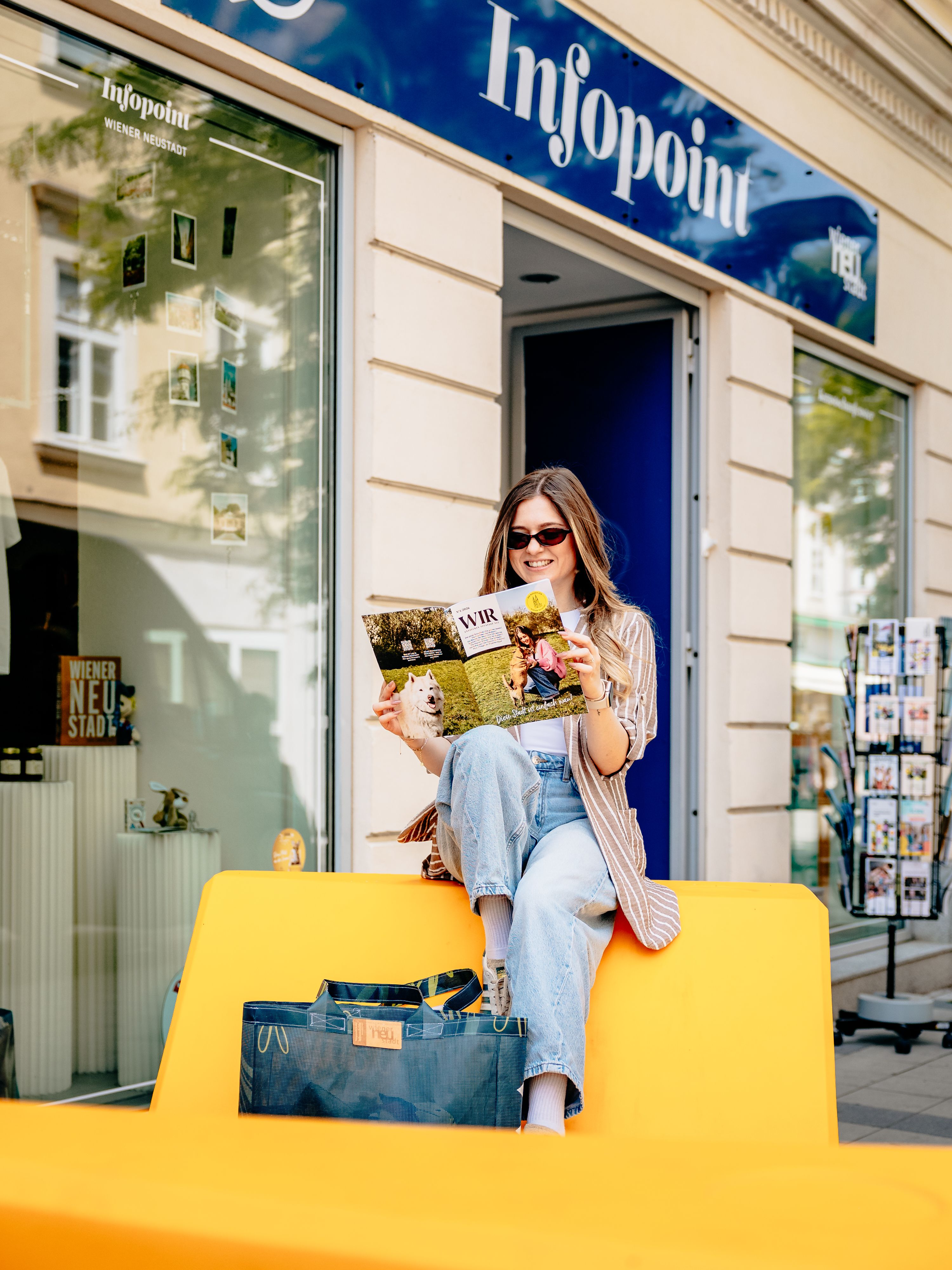Colorful Enzis in front of the information desk, where a woman is reading a city magazine