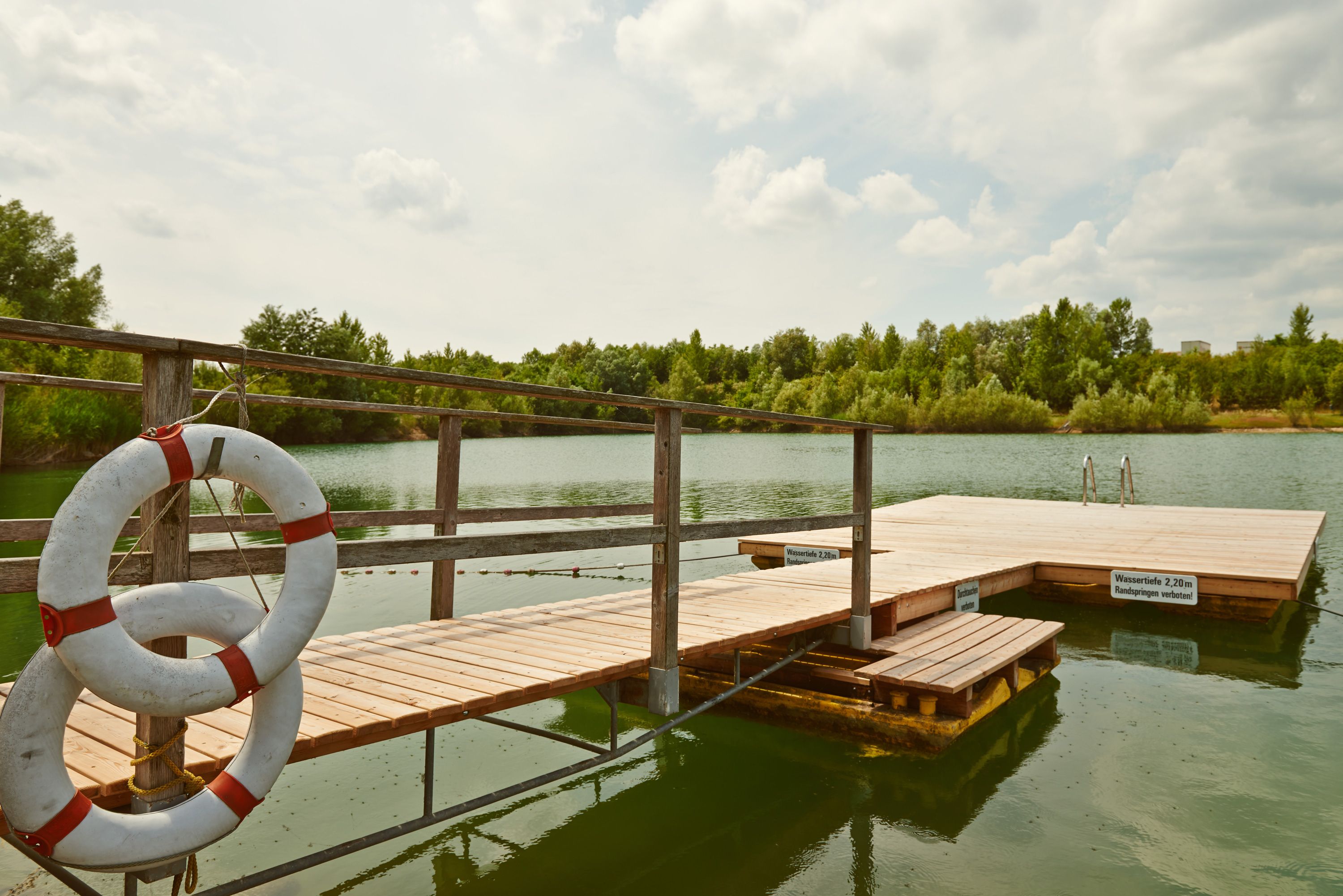 A wooden jetty with lifebuoys on a quiet lake surrounded by trees.