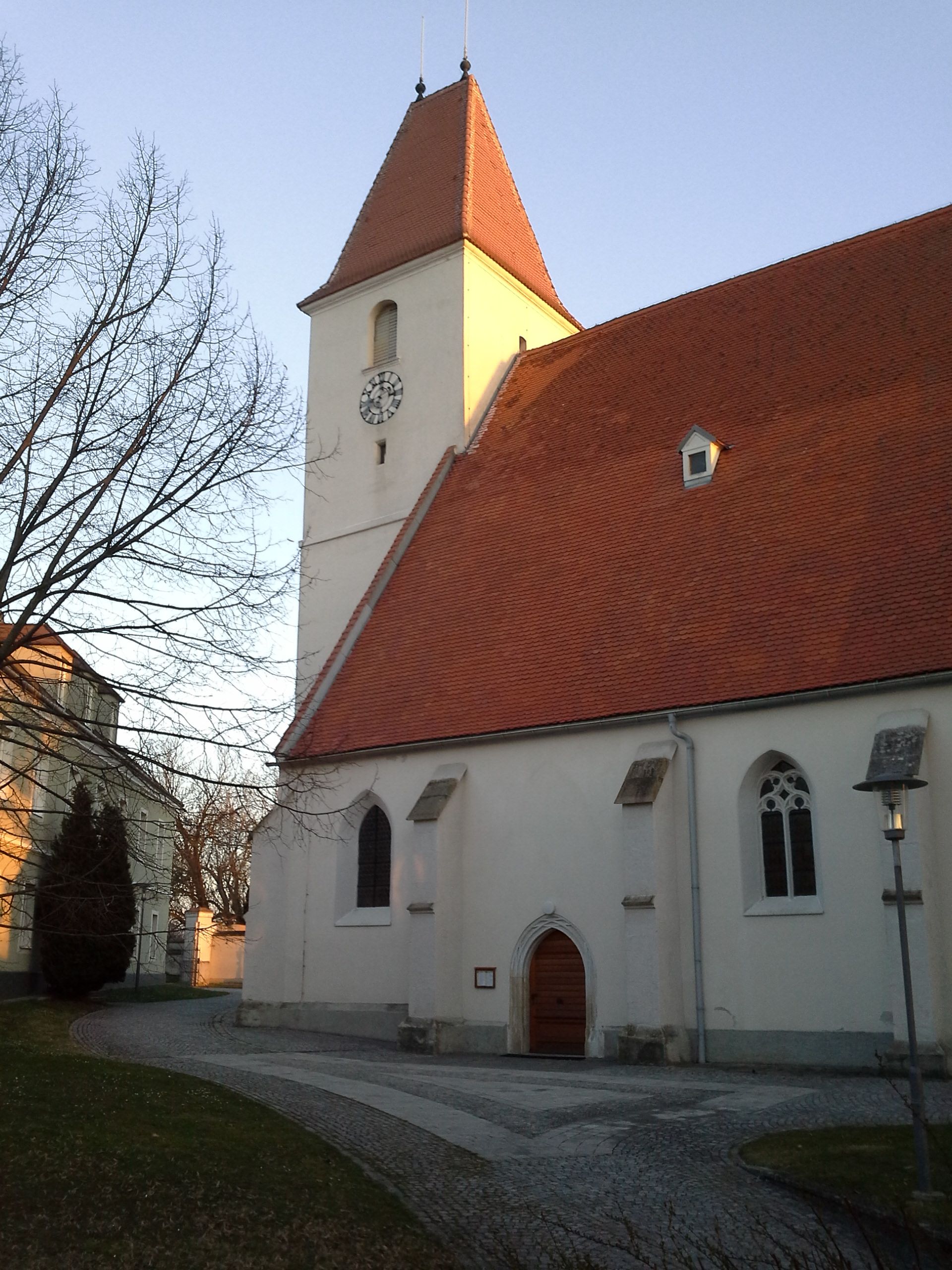Church with red roof and clock tower in Kapelln at sunset.