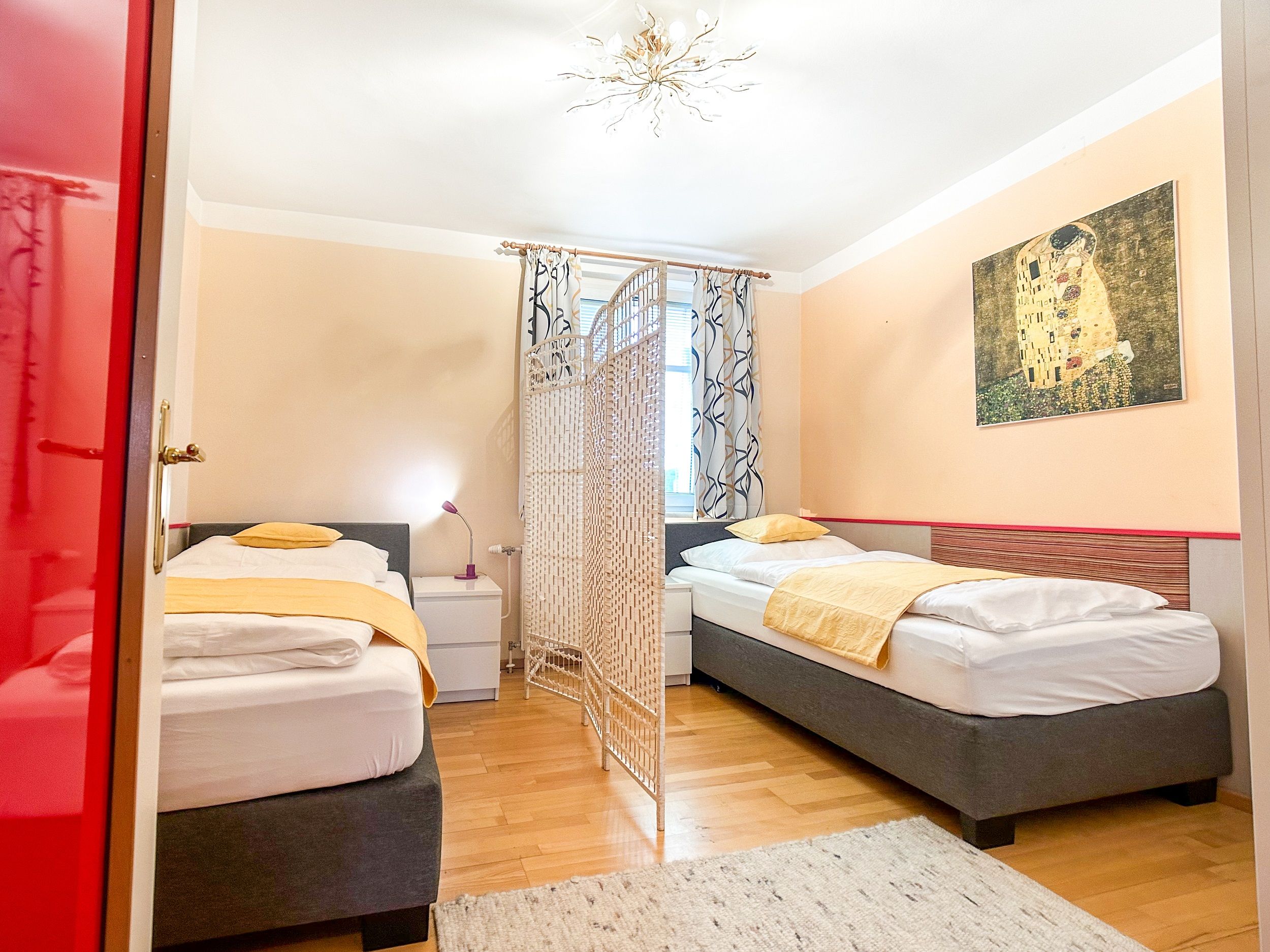 Bedroom with two single beds, yellow bed linen, a room divider and a painting on the wall.