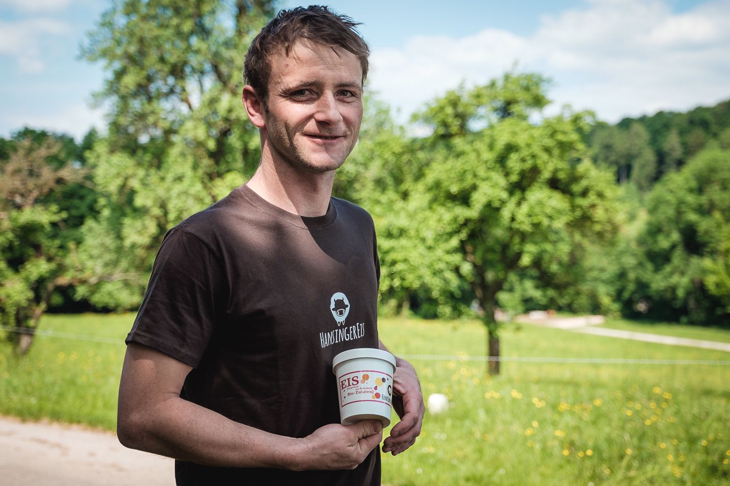 A man holds a cup of organic ice cream in a green landscape.