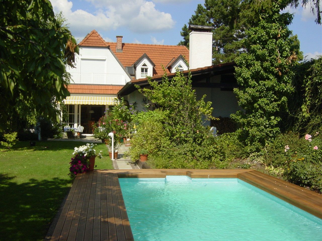 A garden with a pool, surrounded by plants and a house in the background.