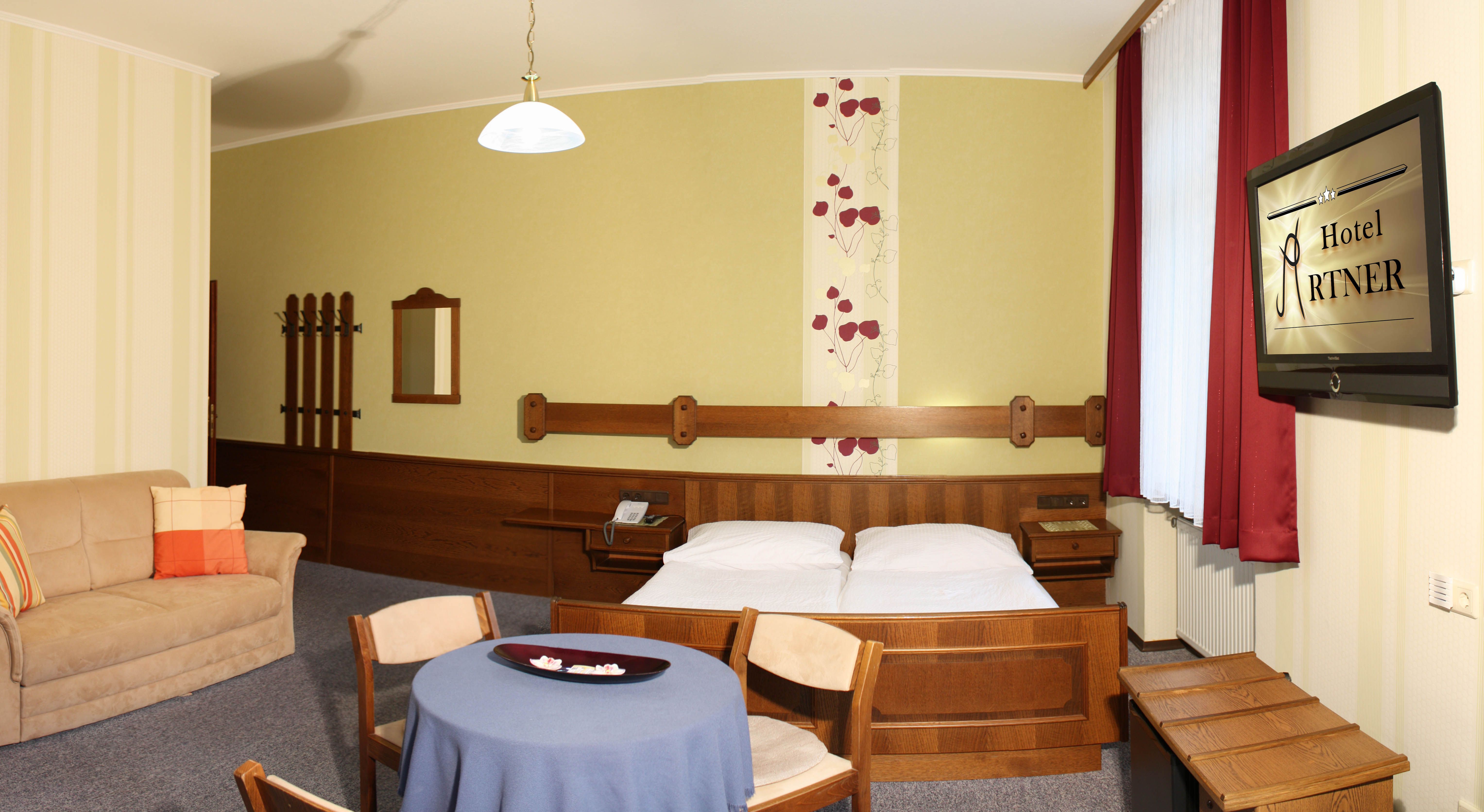 Hotel room with double bed, sofa, table and TV.