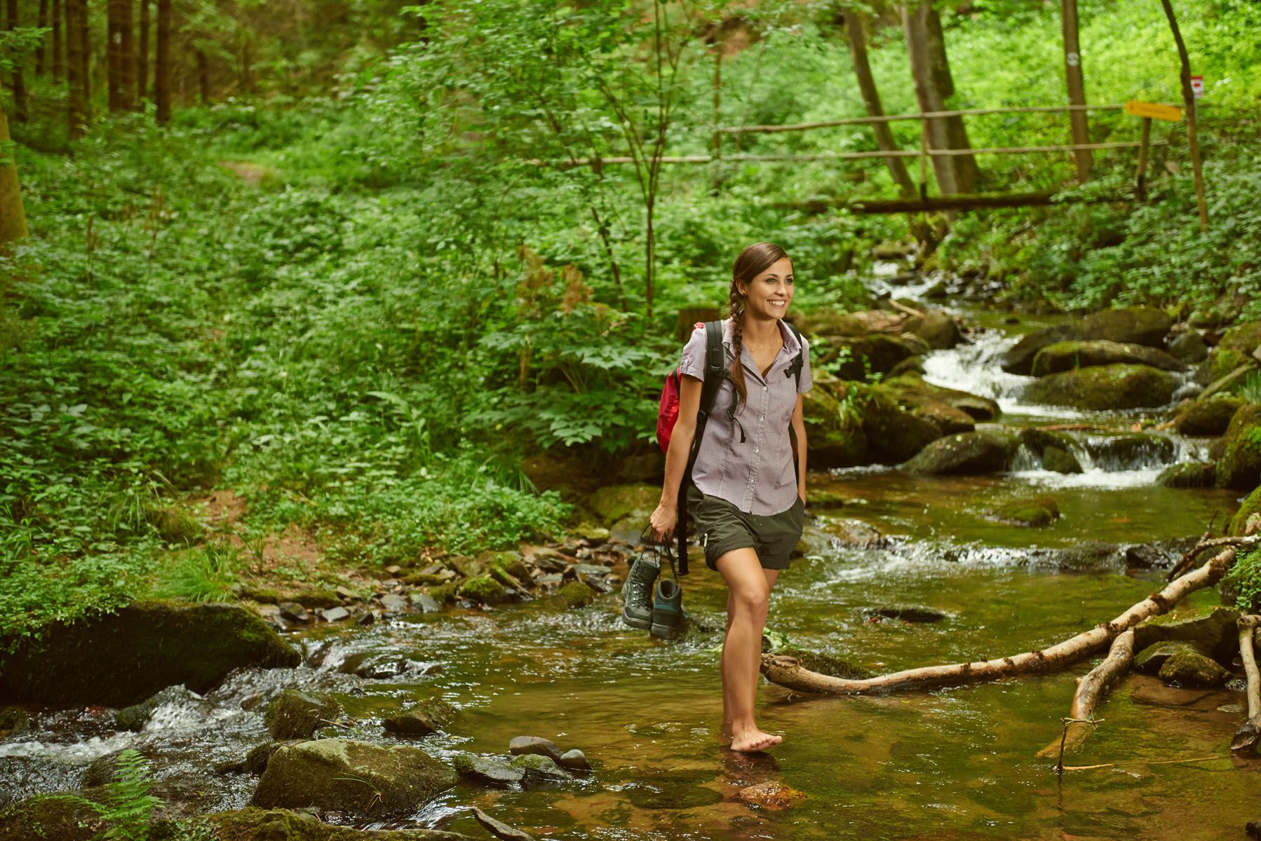 Woman walking barefoot through a stream in a forest.