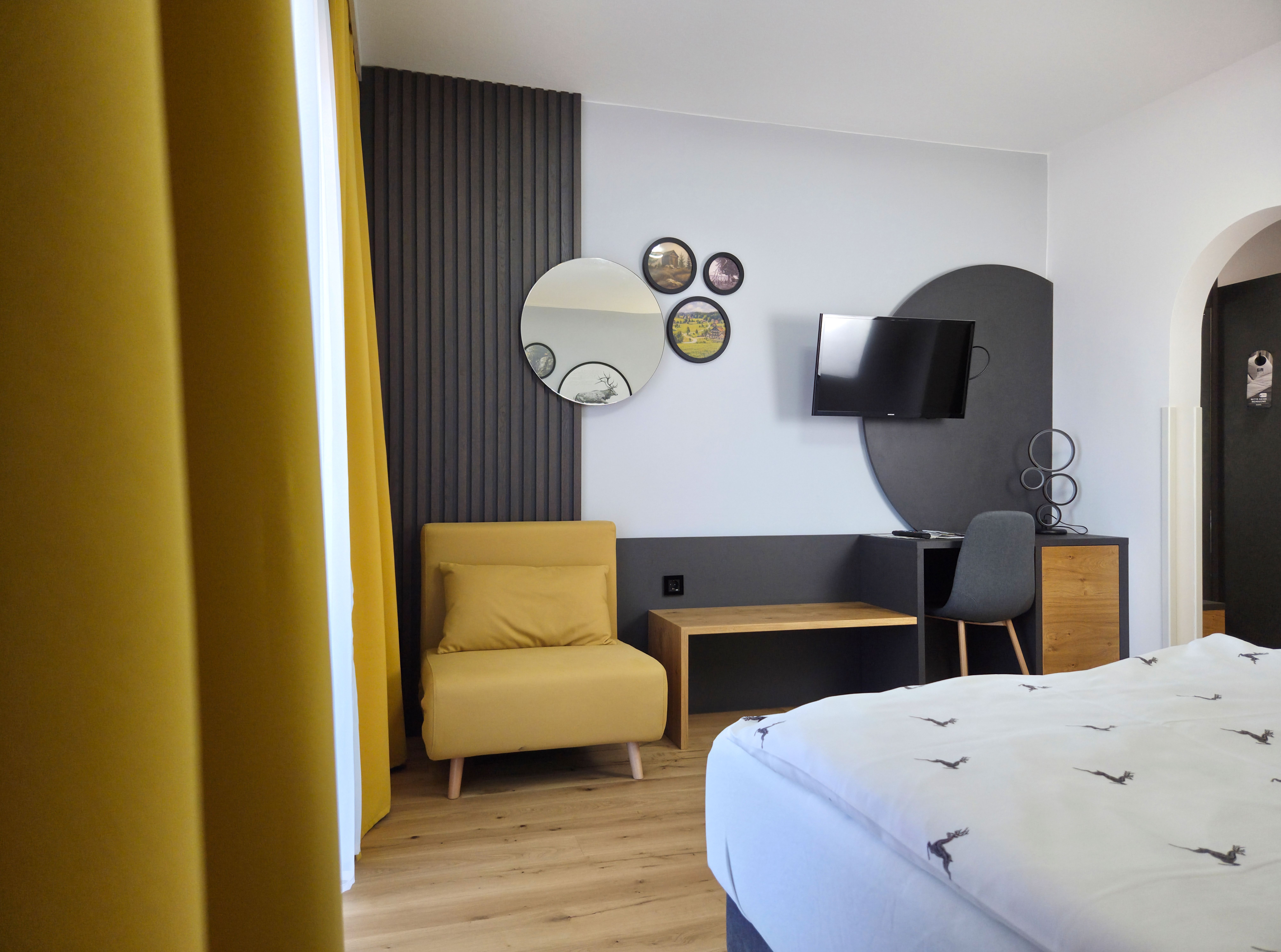 Modernly furnished room with a yellow armchair, mirrors on the wall, a TV and a desk with chair.