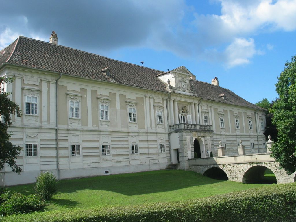 Rohrau Castle with baroque façade and bridge, surrounded by green countryside.