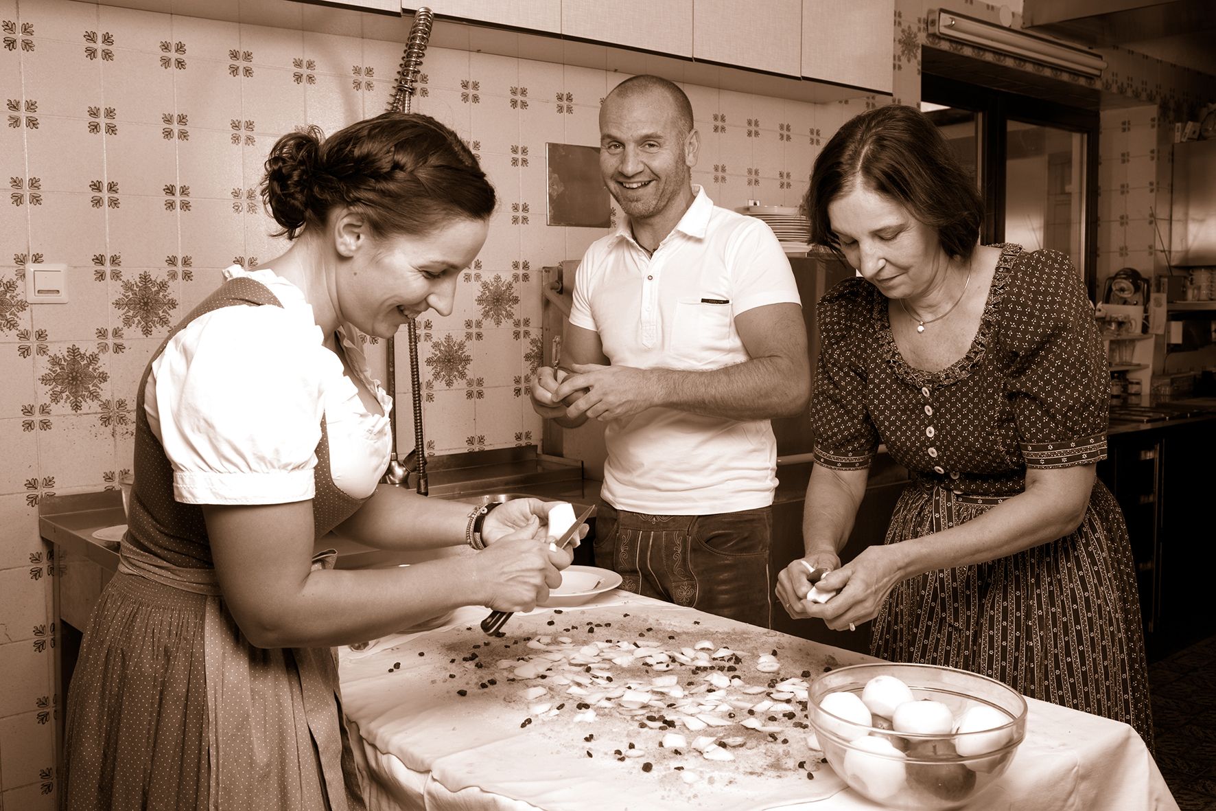 Three people in traditional dress prepare food in a kitchen.