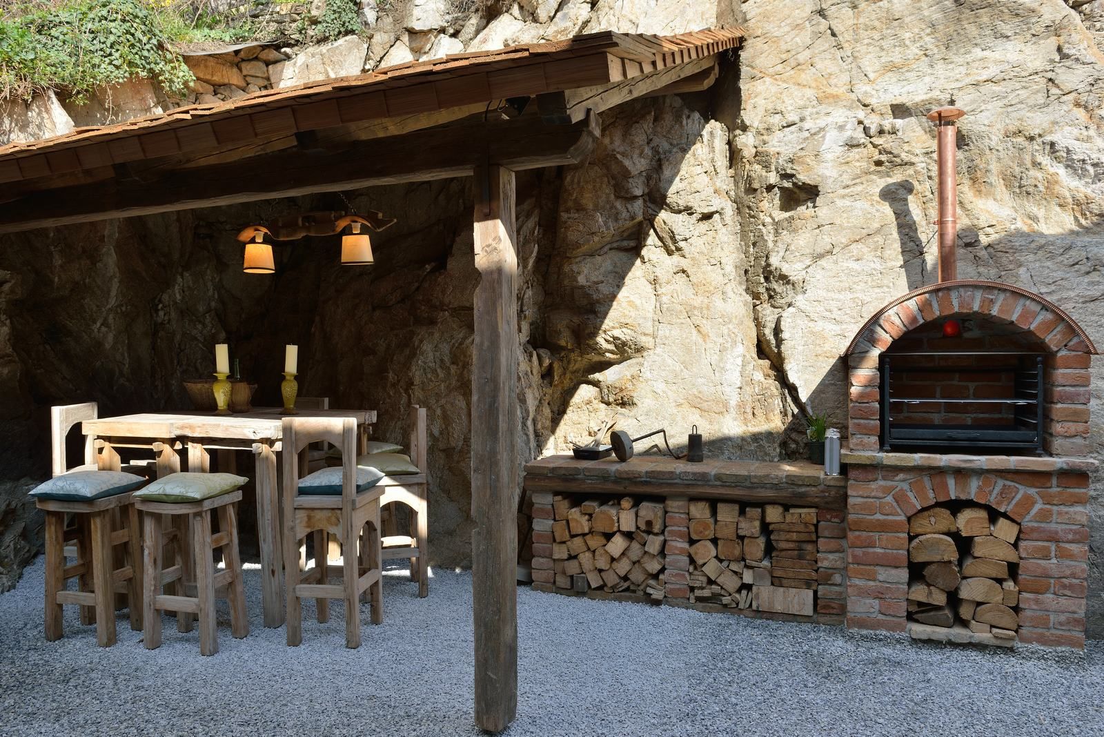 Rustic outdoor area with wooden table, chairs and brick oven.