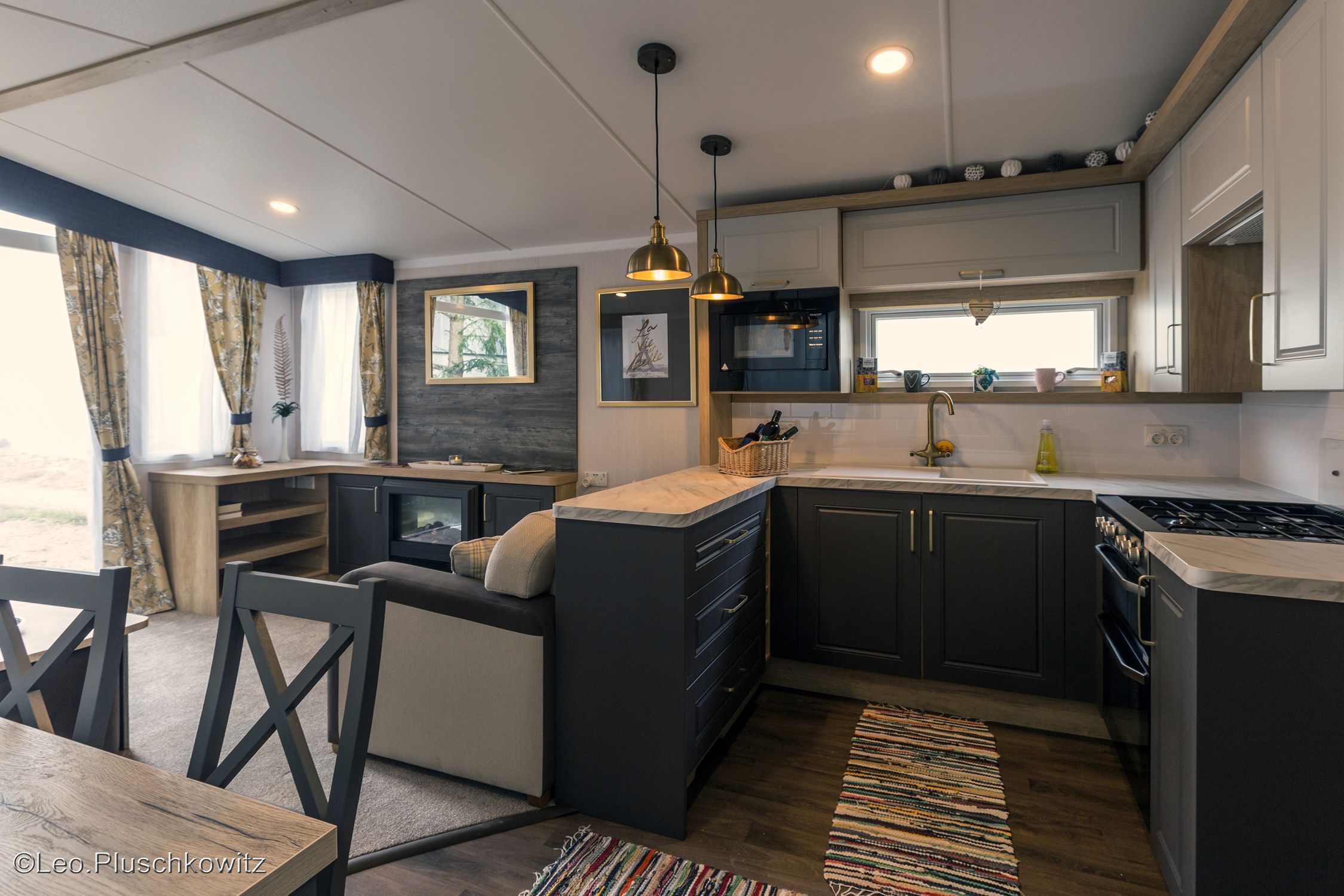 Modern kitchen with dark cupboards, stove, sink and hanging lamps.