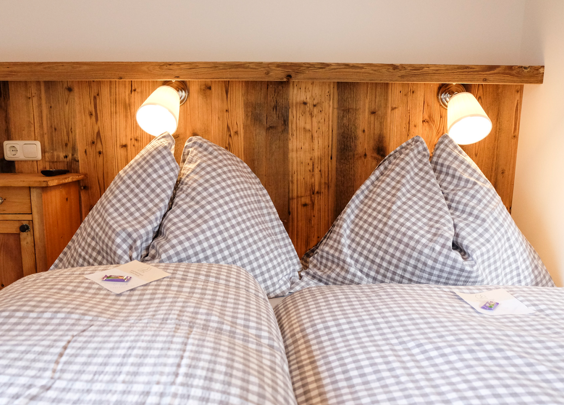 A cozy double bed with checkered duvet covers and two reading lamps mounted on a wooden headboard.