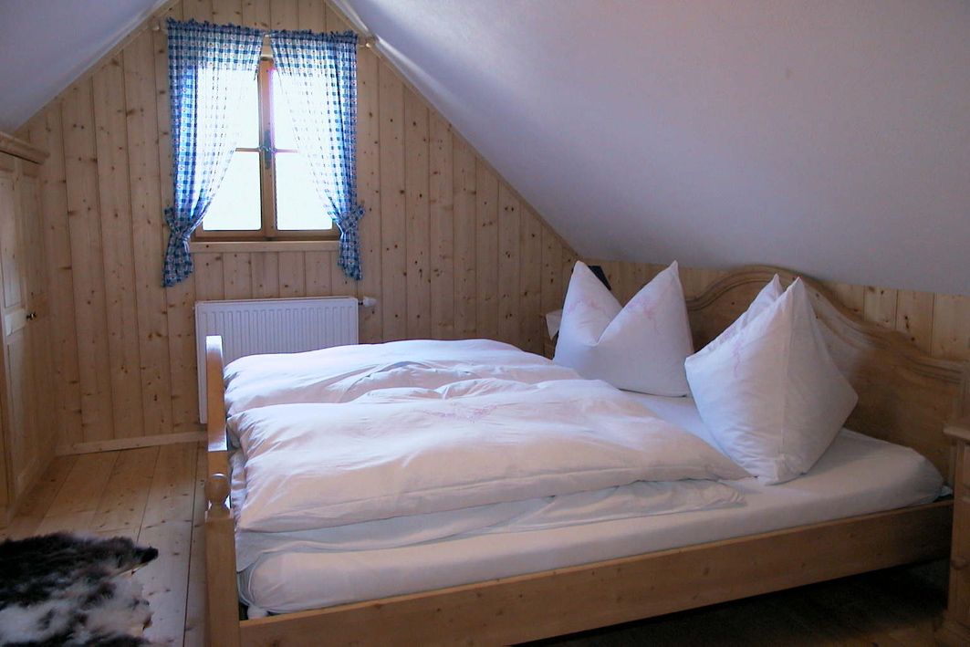 Cozy bedroom with wooden walls, a double bed and a window with blue checkered curtains.