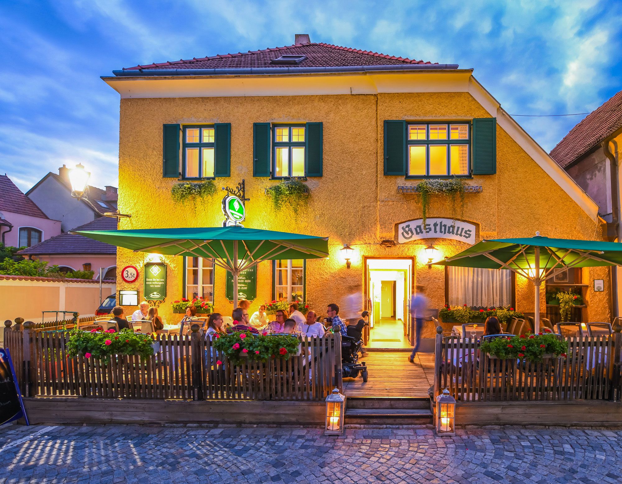 Exterior view of an inn with terrace and guests at dusk.