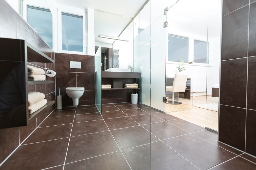 Modern bathroom with dark tiles, glass walls and white sanitary facilities.