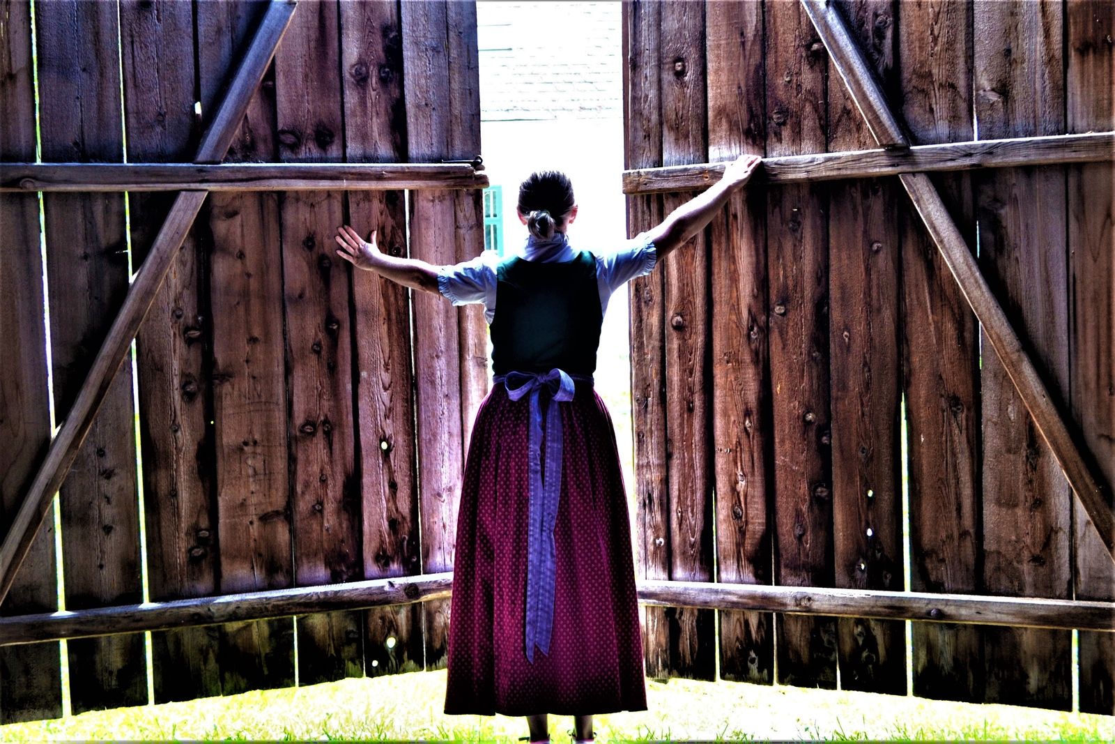 A woman in traditional dress opens large wooden doors to the outside.