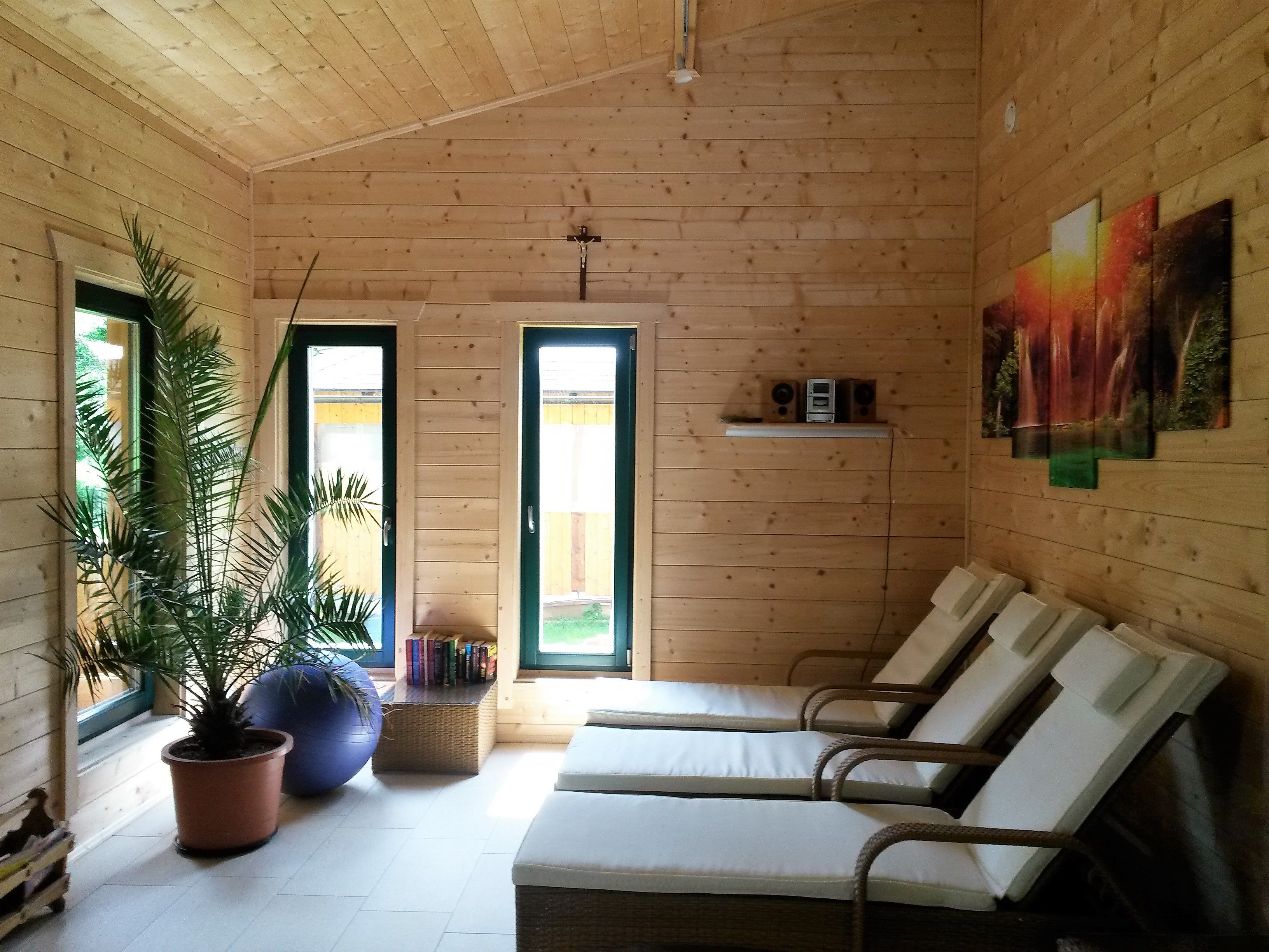 Interior of a sauna with wooden paneling, loungers, a palm tree and a picture on the wall.