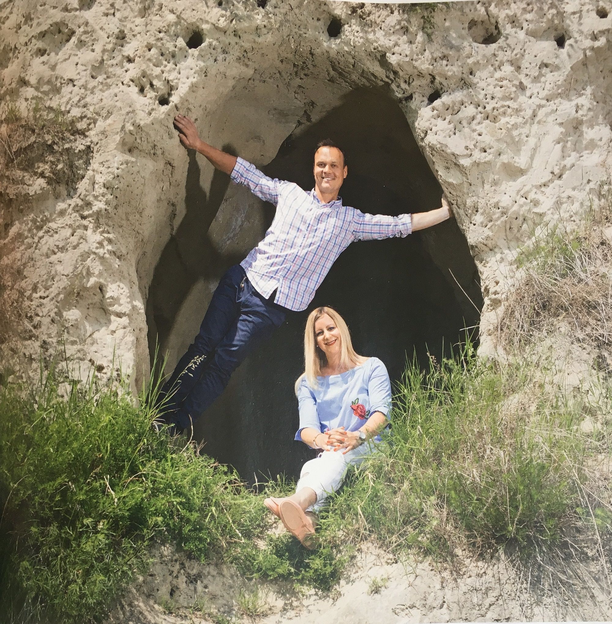 Two people pose in front of a rock cave.
