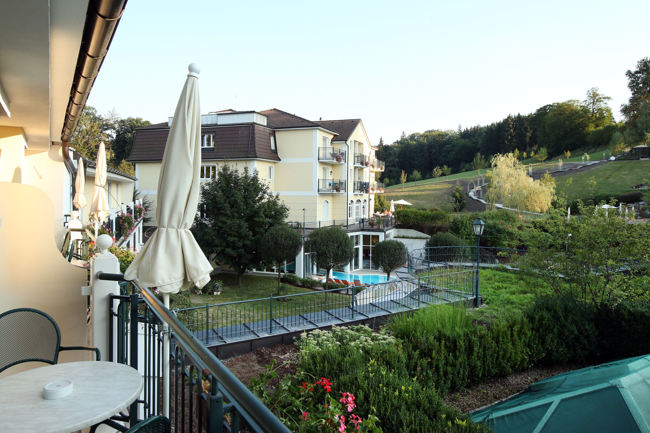 A hotel in the middle of a green landscape with a pond and sun loungers.