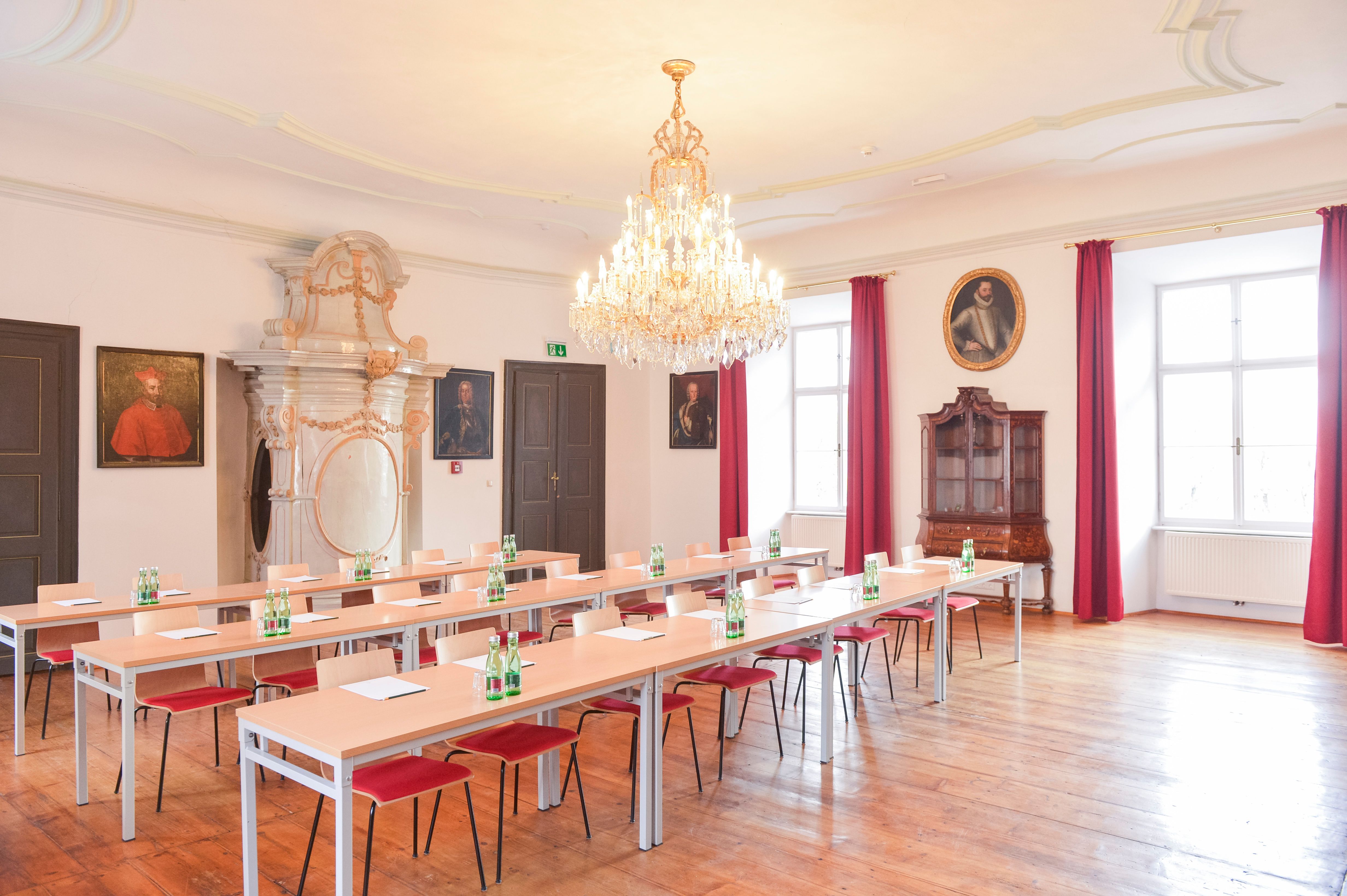 Elegant seminar room with chandelier, wooden floor and portraits on the walls.