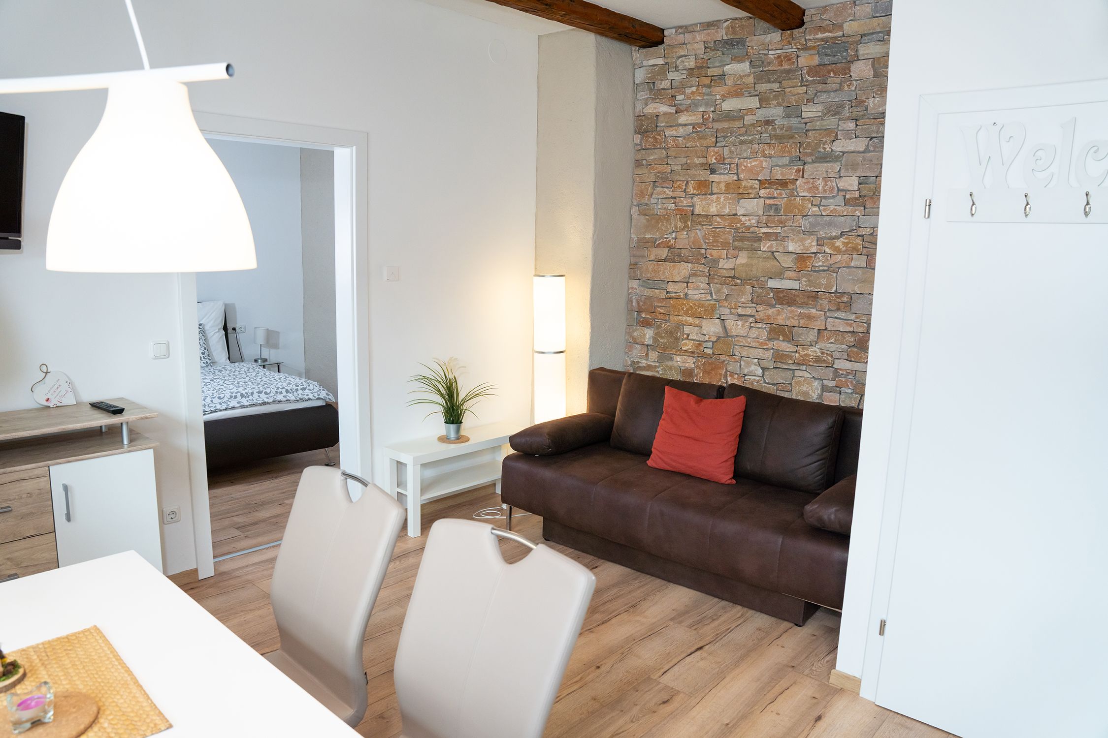Modern living room with brown sofa, stone wall and view into the bedroom.