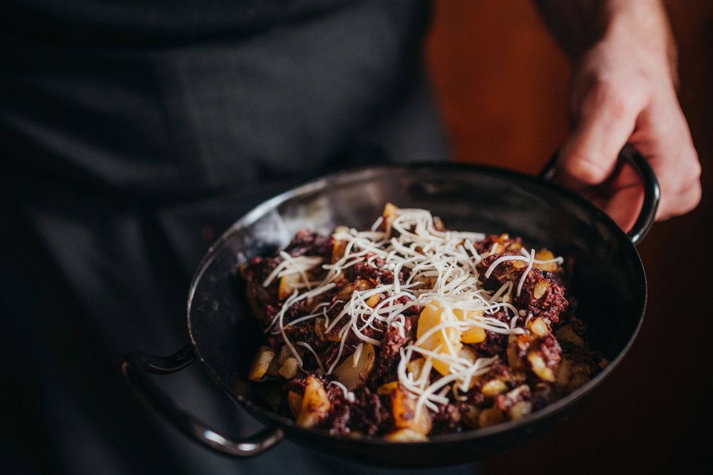One person holds a pan of Blunzengröstl, garnished with grated cheese.