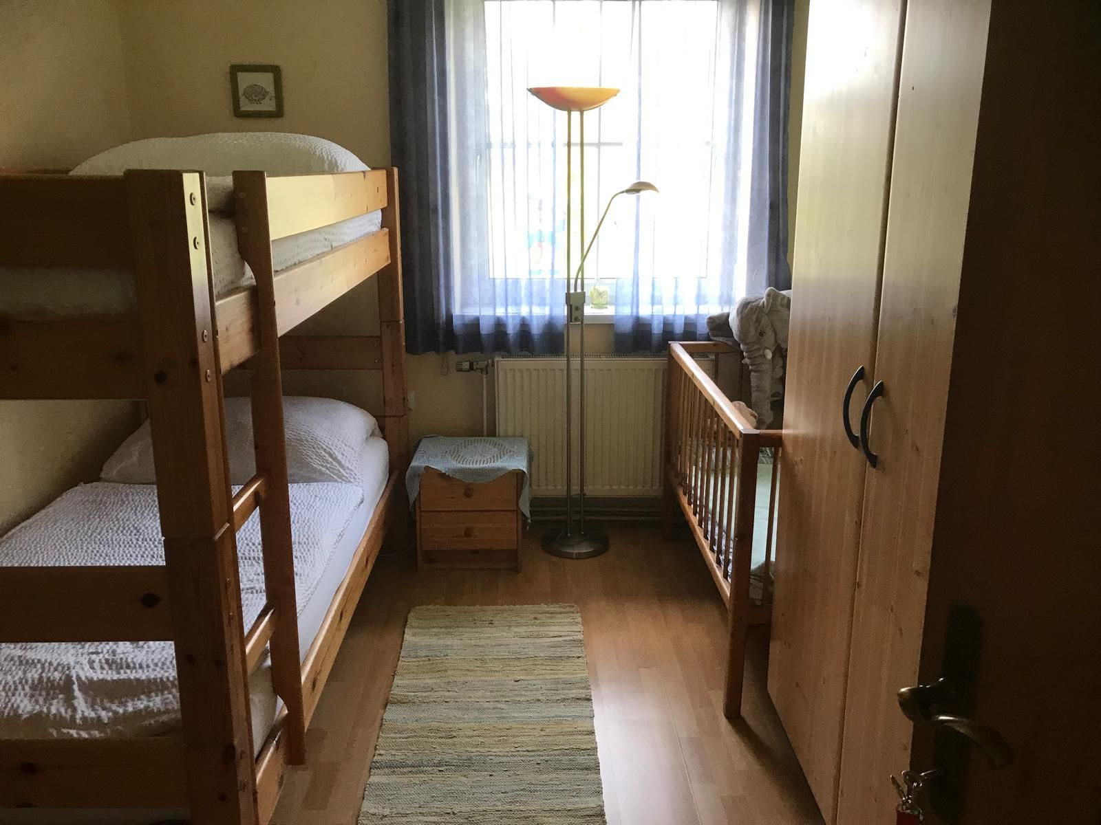 Children's room with bunk bed, crib, wardrobe and floor lamp.