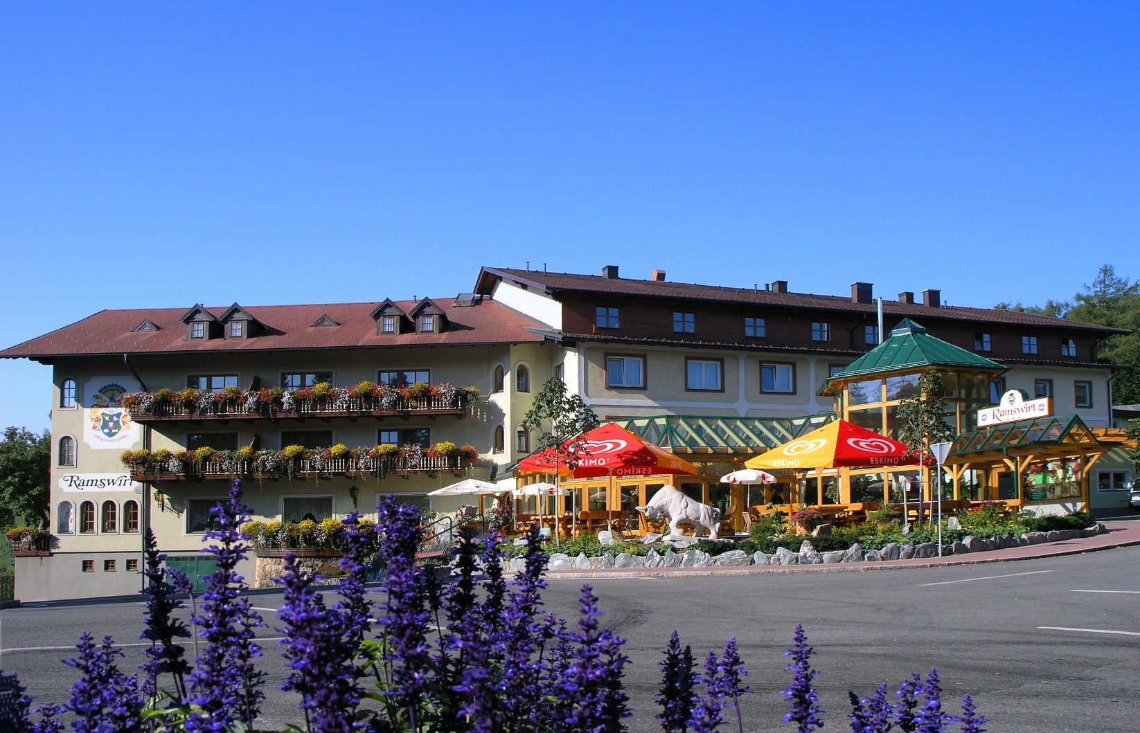 Gasthof Ramswirt with flowering balconies and parasols against a blue sky.