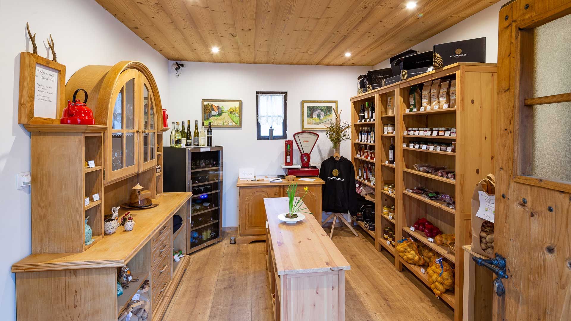 Interior view of a small, cozy store with wooden shelves filled with regional products such as wine, jam and vegetables.