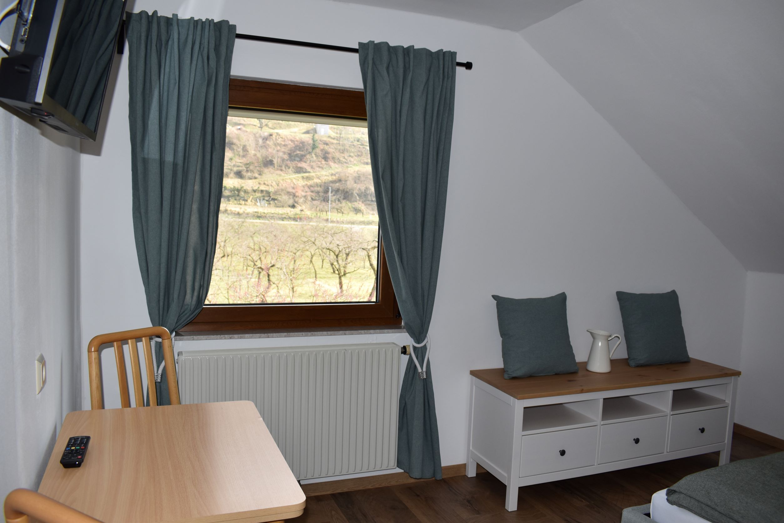 Interior view of a room with window, table, chair and chest of drawers.