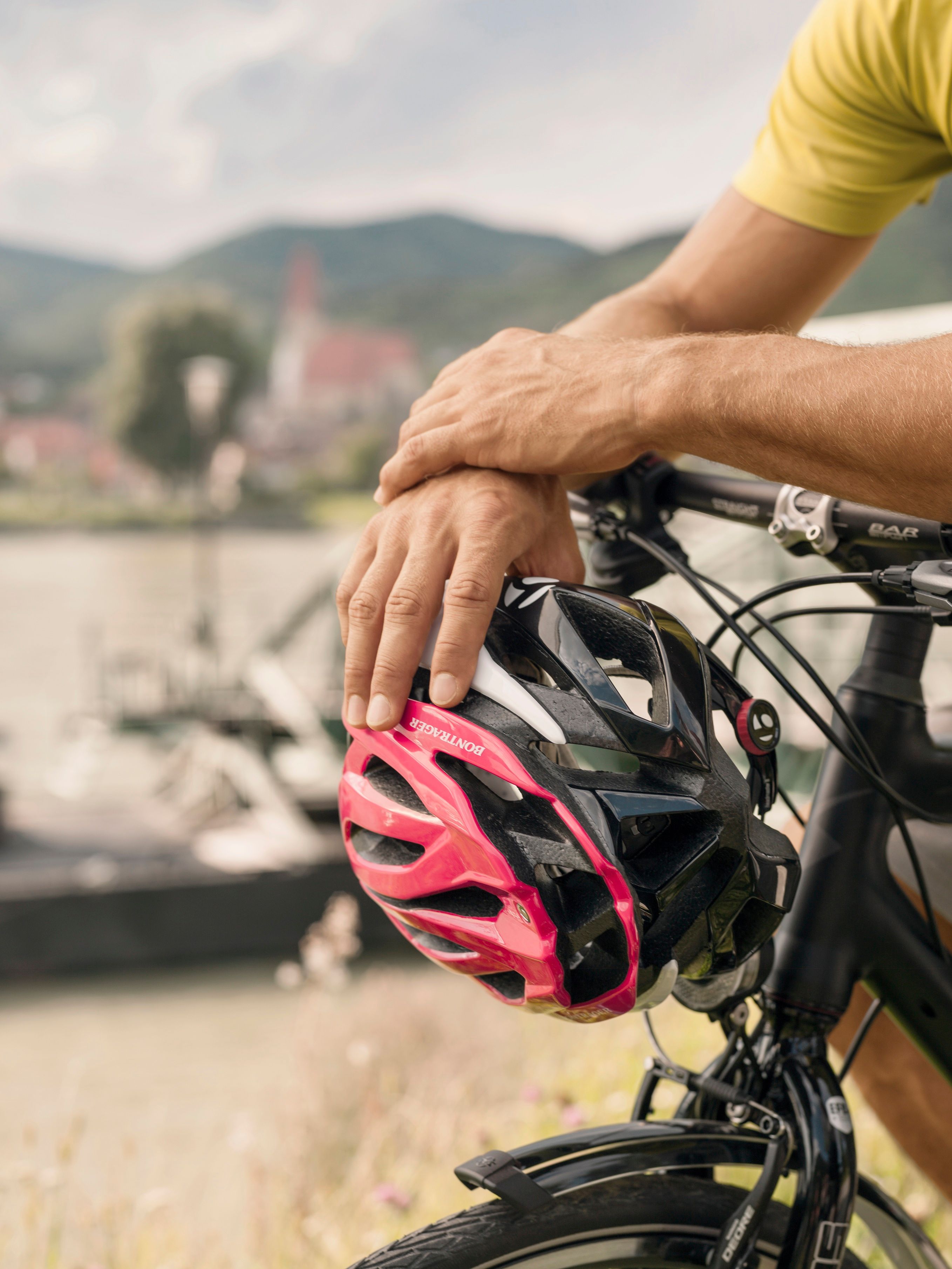 Two hands holding a bicycle helmet on a bicycle handlebar