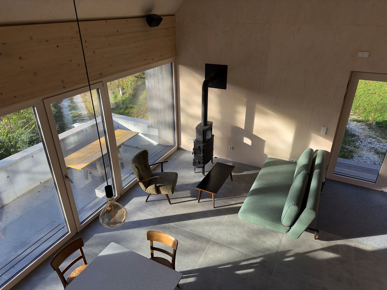 Modern living and dining area with large windows, sofa, armchair and fireplace.