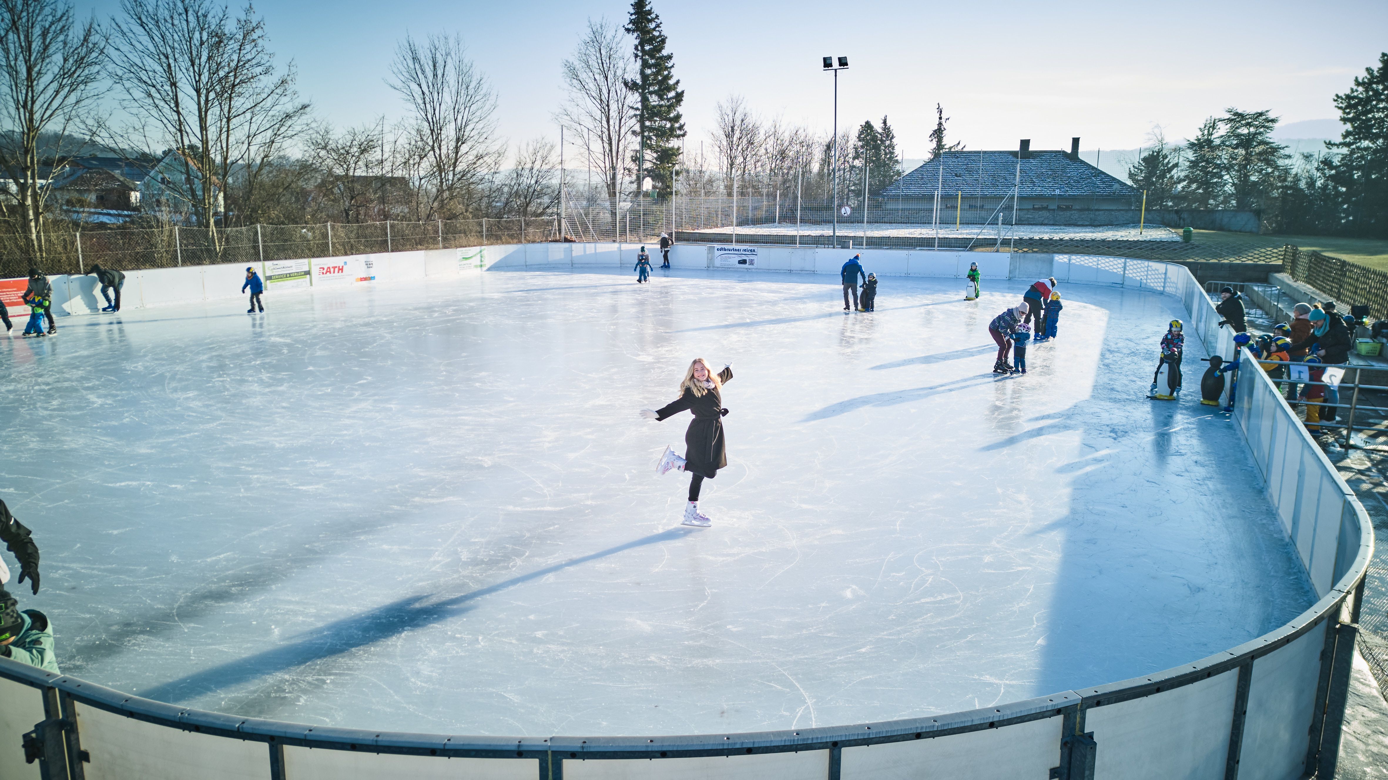 People skating on an open-air ice rink with trees in the background.