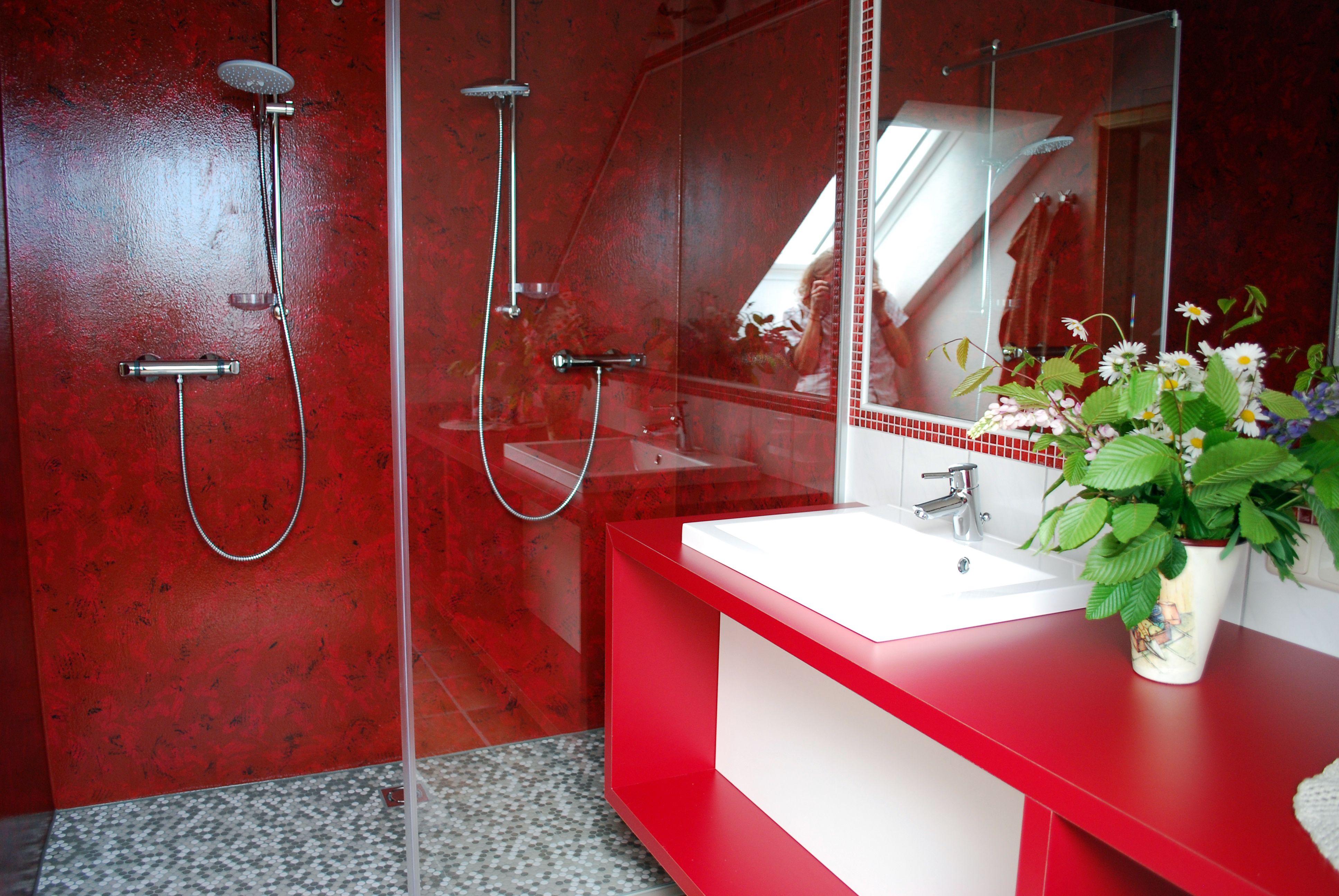 Modern bathroom with red walls, two showers and a washbasin with floral arrangement.