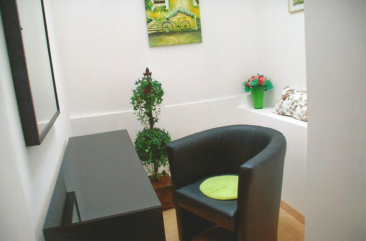 Small guest room with black armchair, green cushion, mirror, plants and mural.