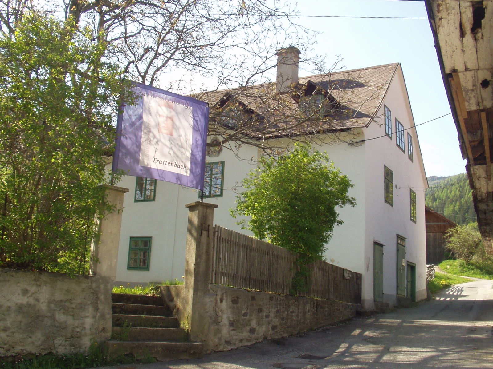 A white building with green window frames and a sign saying 'Trattenbach'.