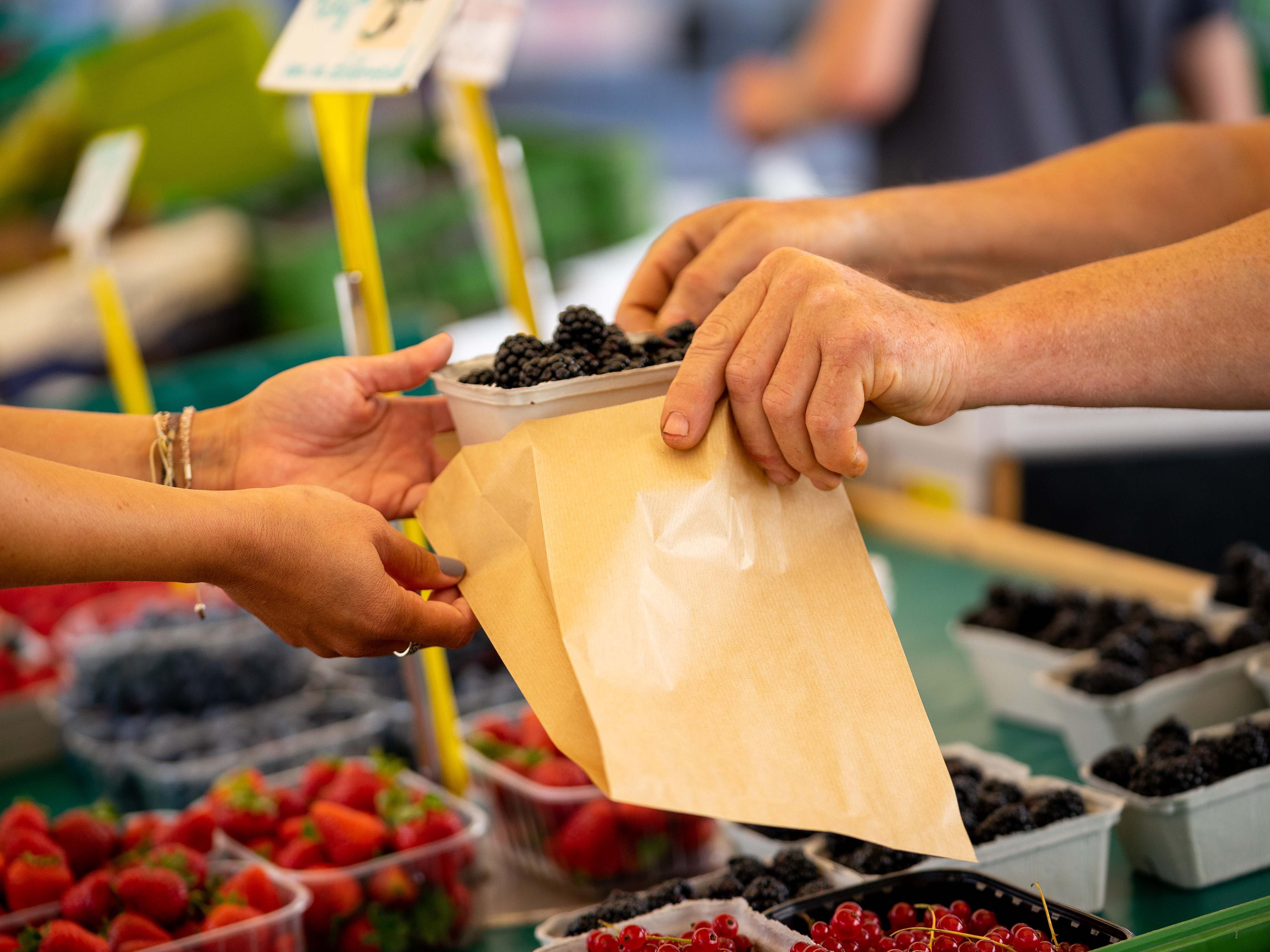 Close-up of hands handing berries into a paper bag at a market.