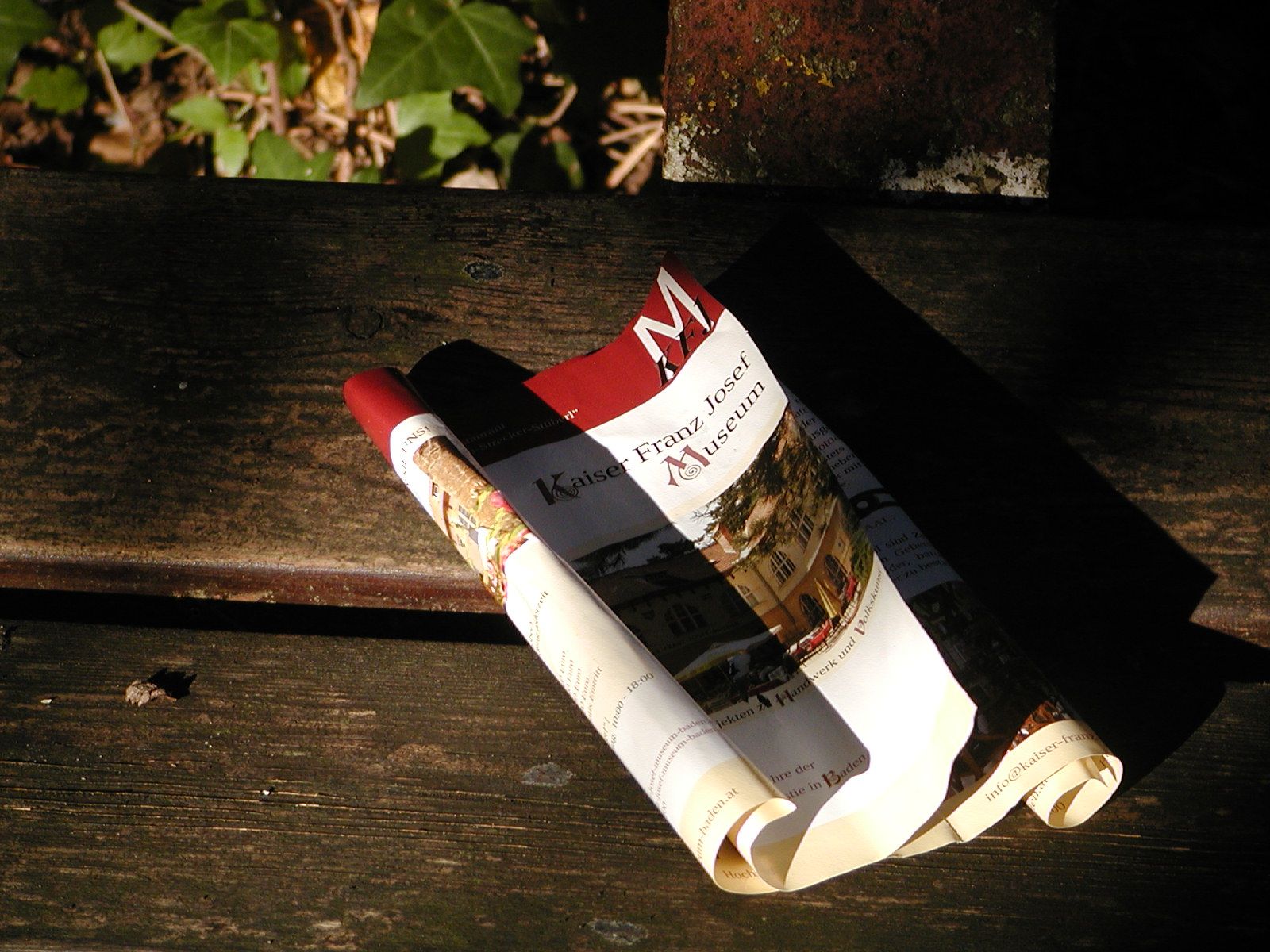 Rolled up brochure of the Kaiser-Franz-Josef-Museum on a wooden bench.