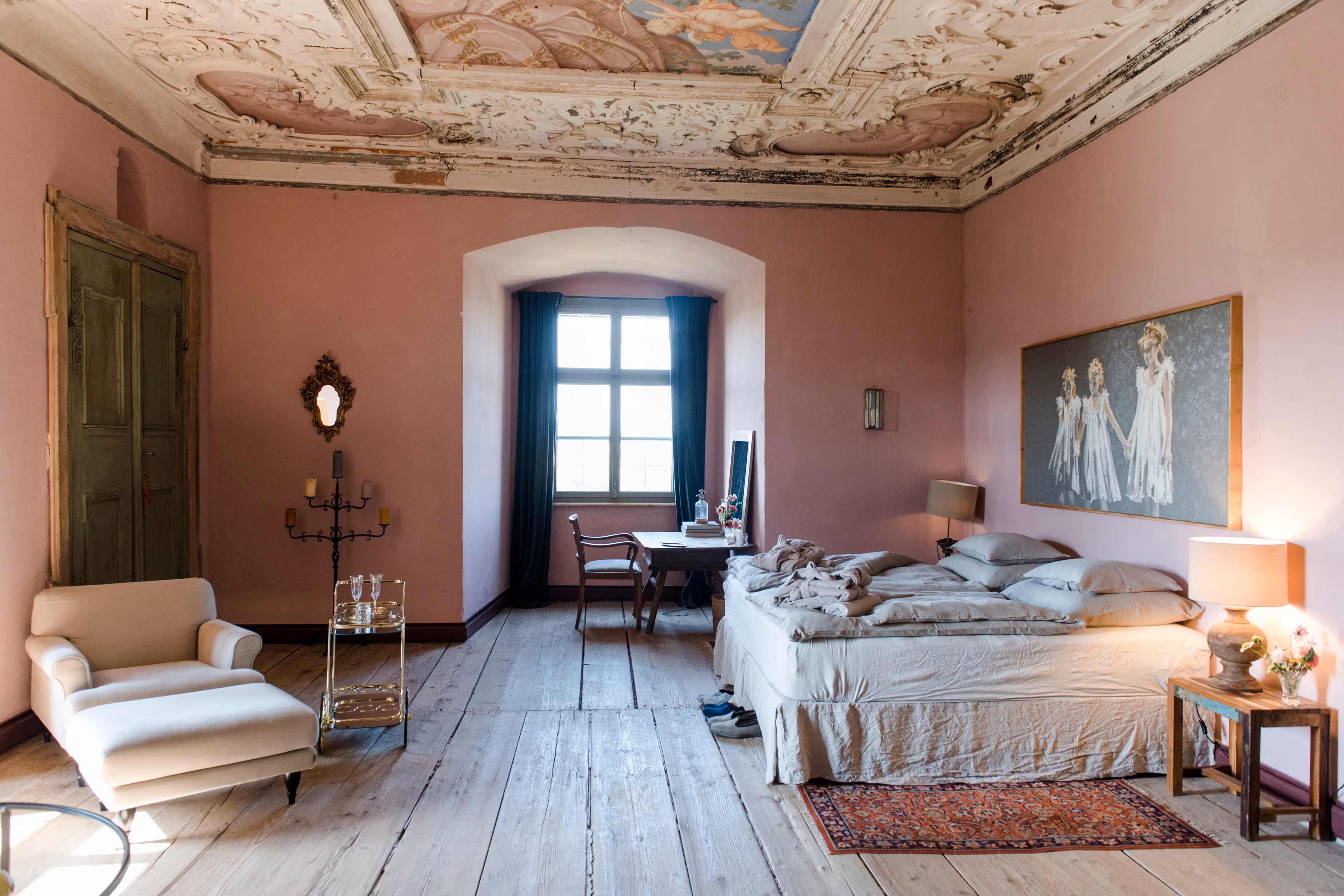 Elegant bedroom with antique ceiling, pink walls and wooden floor.