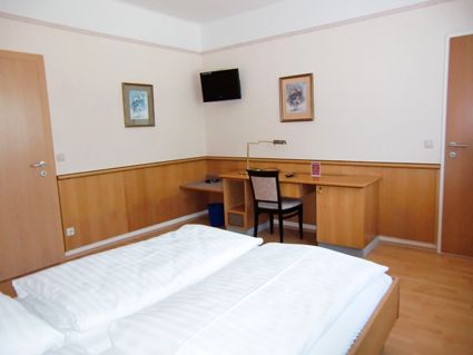 A hotel room with double bed, desk, chair and wall decoration.