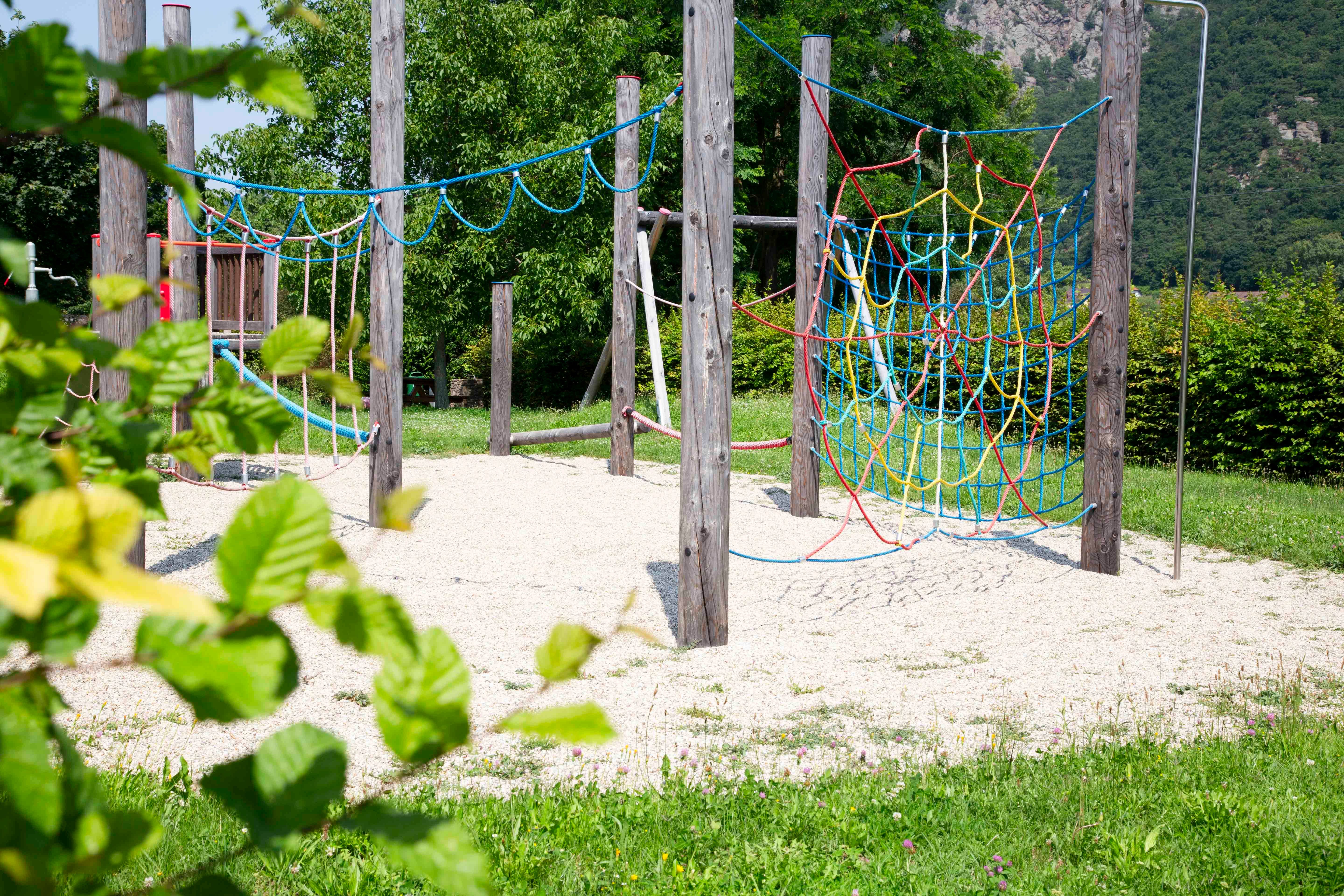 An adventure playground with climbing ropes and wooden poles, surrounded by green nature.
