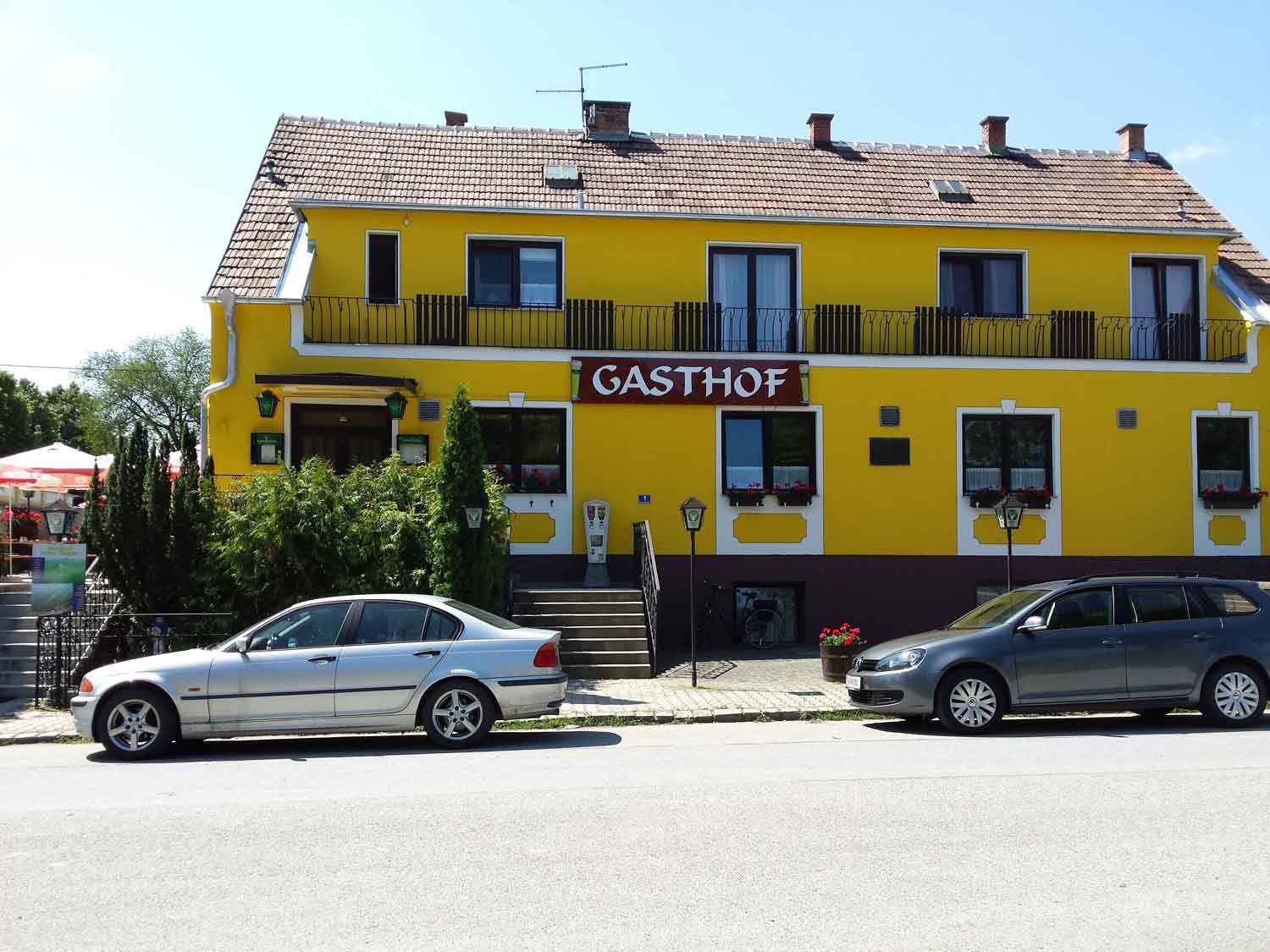Yellow building with the sign 'Gasthof', two cars parked in front of it.