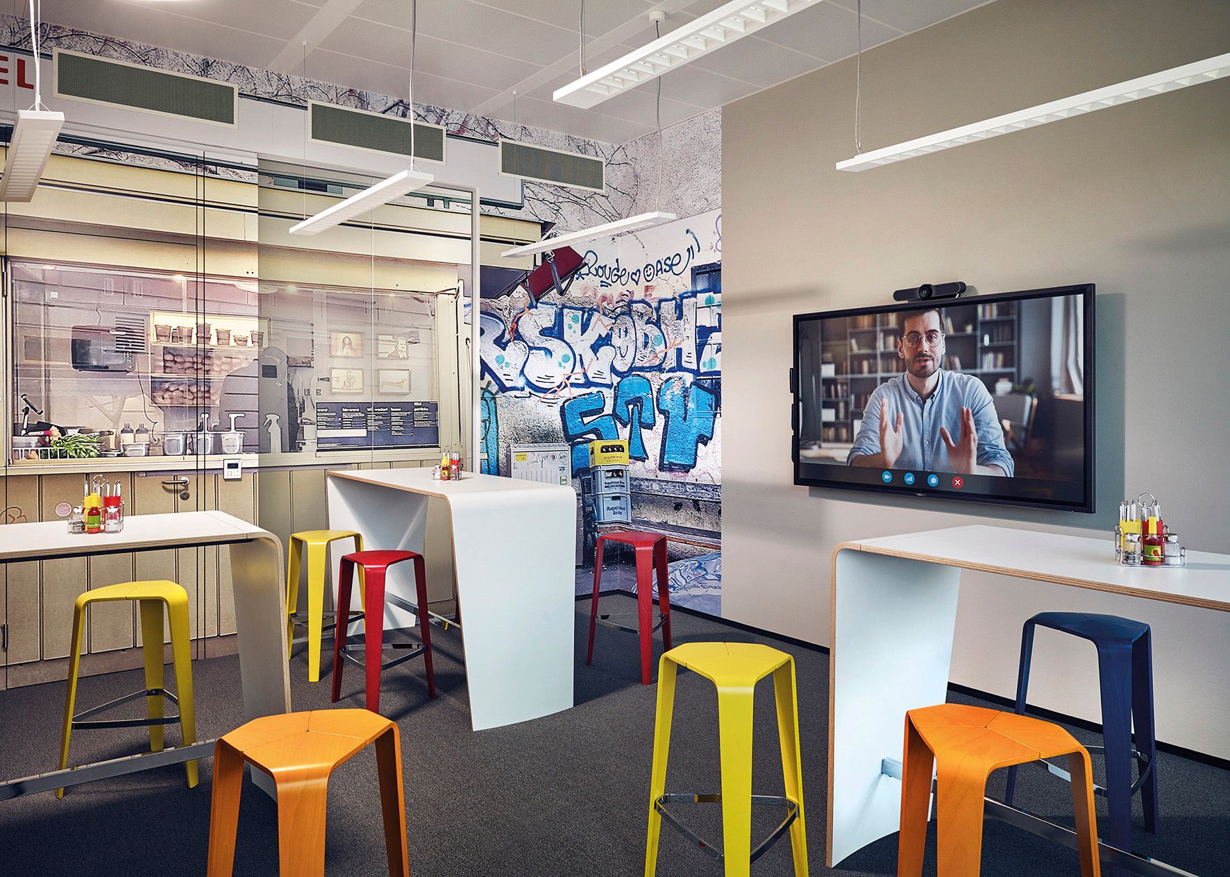 Modern conference room with graffiti wall, colorful stools and video conference screen.