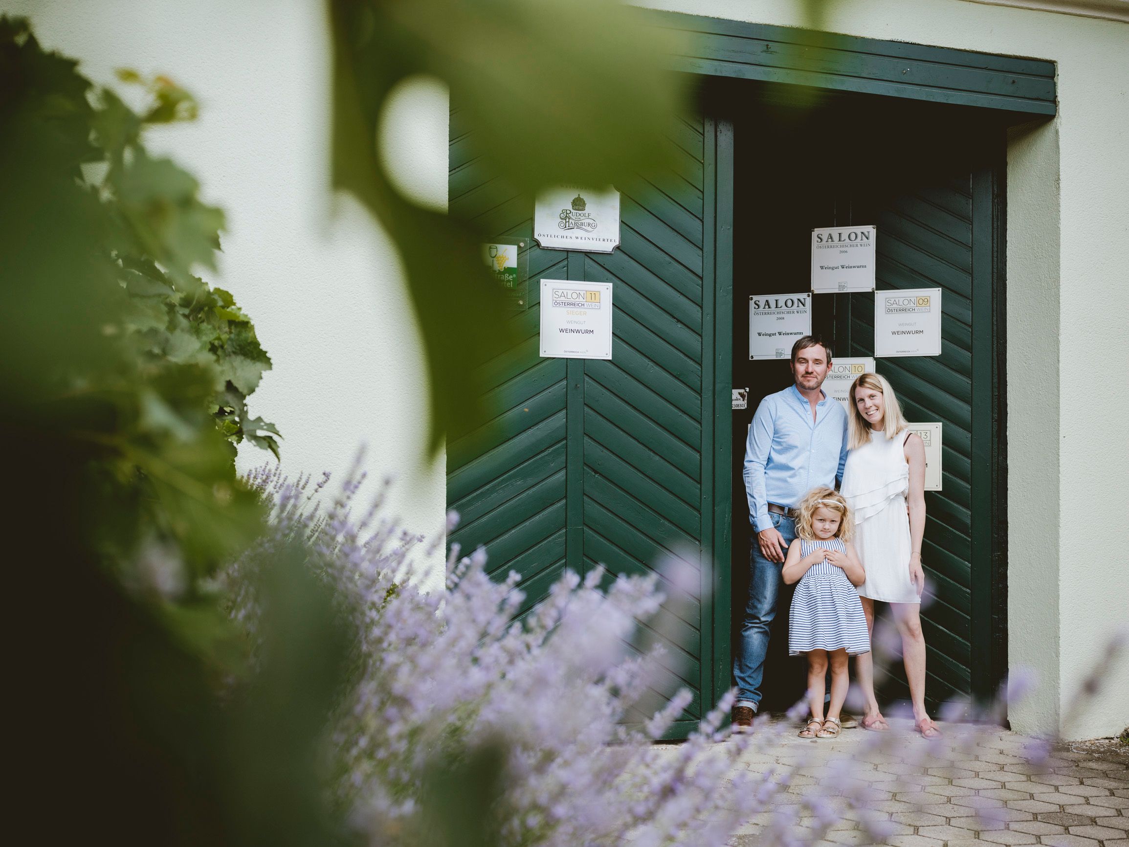 A family stands in front of a green gate, surrounded by lavender and plants.