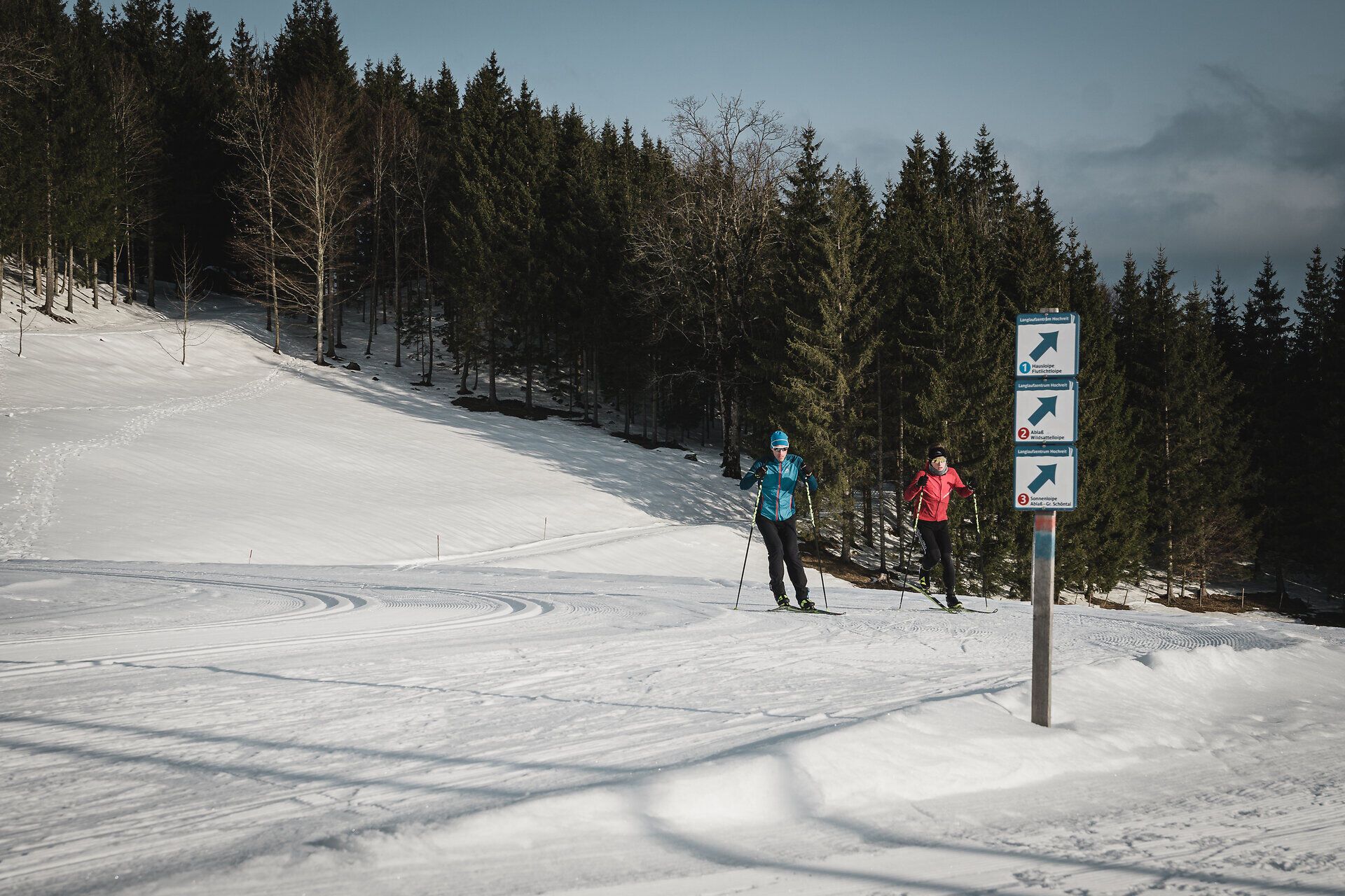 Die glitzernde Schneedecke erstreckt sich über die sanften Hügel der Ybbstaler Alpen, während zwei Langläufer in lebhaften Farben die ruhige Winterlandschaft durchqueren. Die frische, klare Luft und die majestätischen Tannen schaffen eine perfekte Kulisse für ein unvergessliches Winterabenteuer.