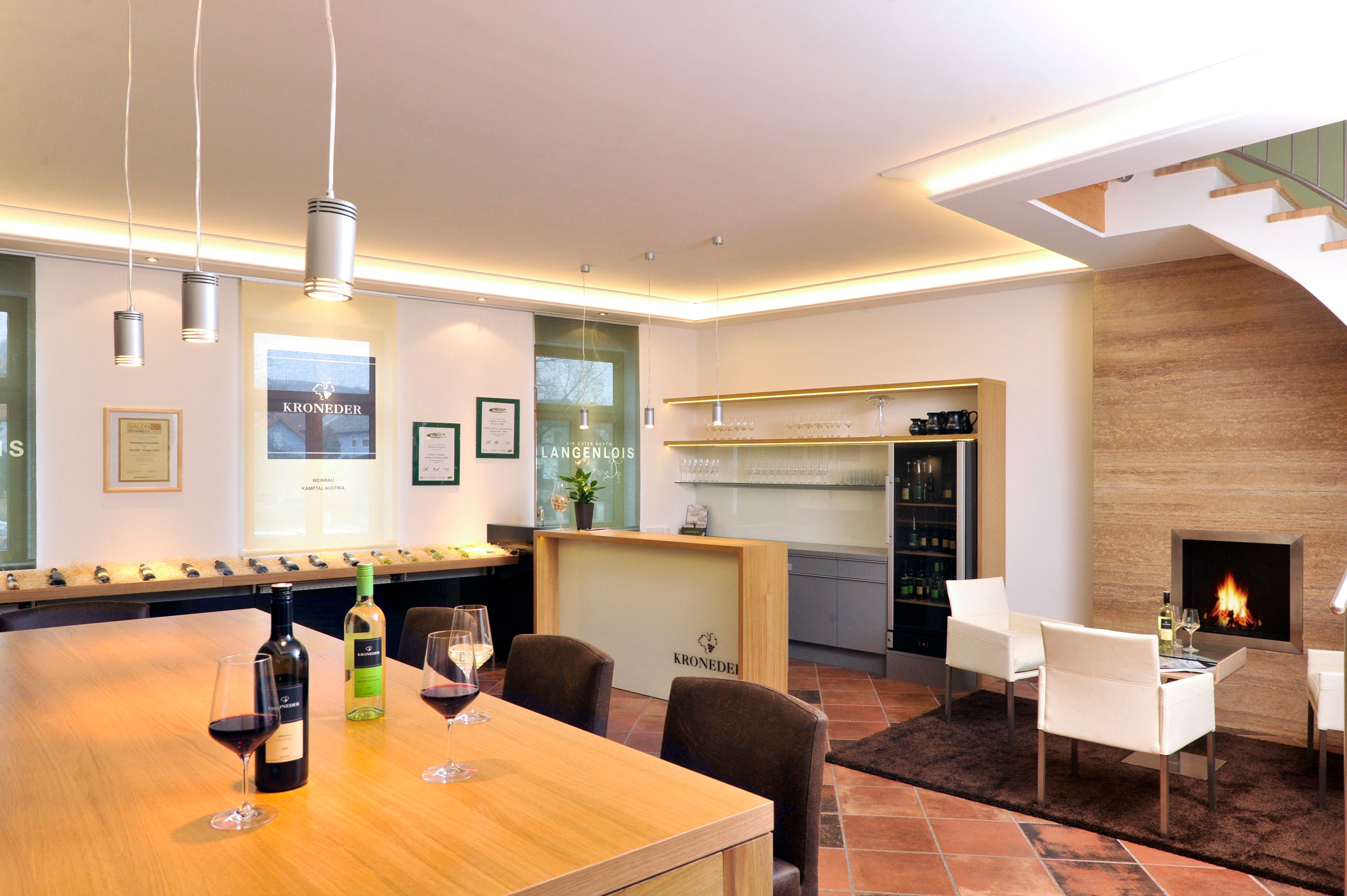 Interior view of a modern wine tasting room with wooden table, wine glasses, fireplace and shelves.