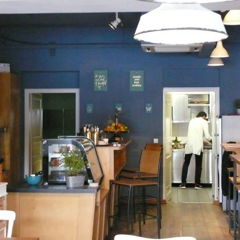 Interior view of a café with blue wall, counter, bar stools and a person in the kitchen.