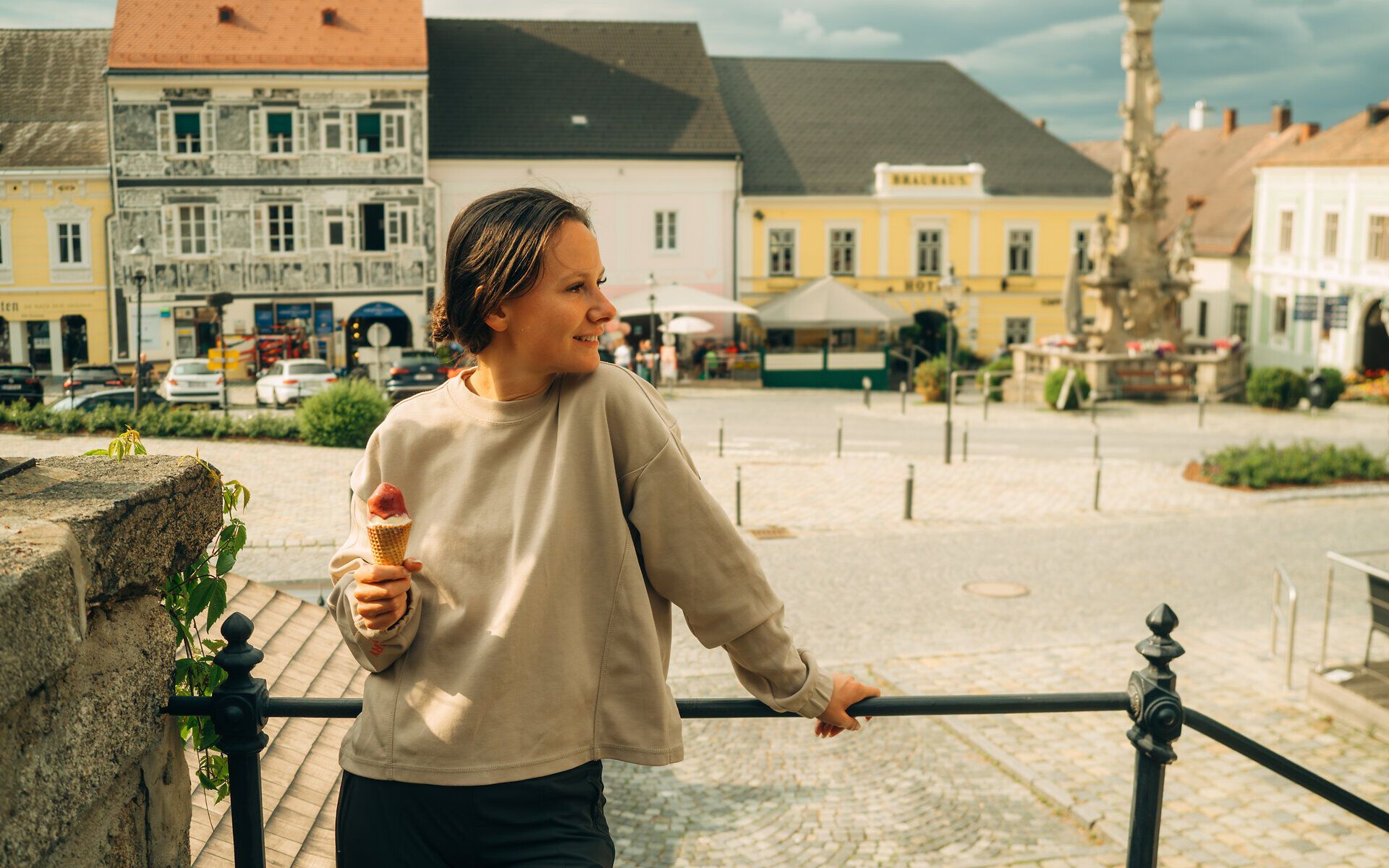 A woman stands in front of a railing and looks out onto the main square in Weitra, holding an ice cream in her hand.