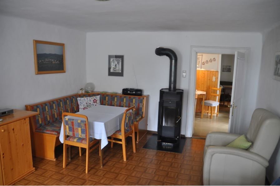 Cozy dining area with corner bench, table and chairs, next to a stove. In the background a passageway to another room.