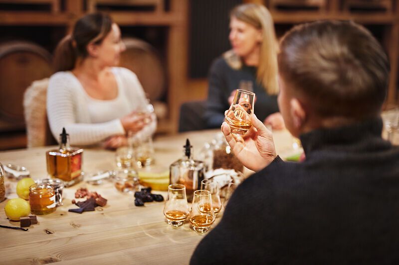 People at a whisky tasting at a table with glasses and ingredients.