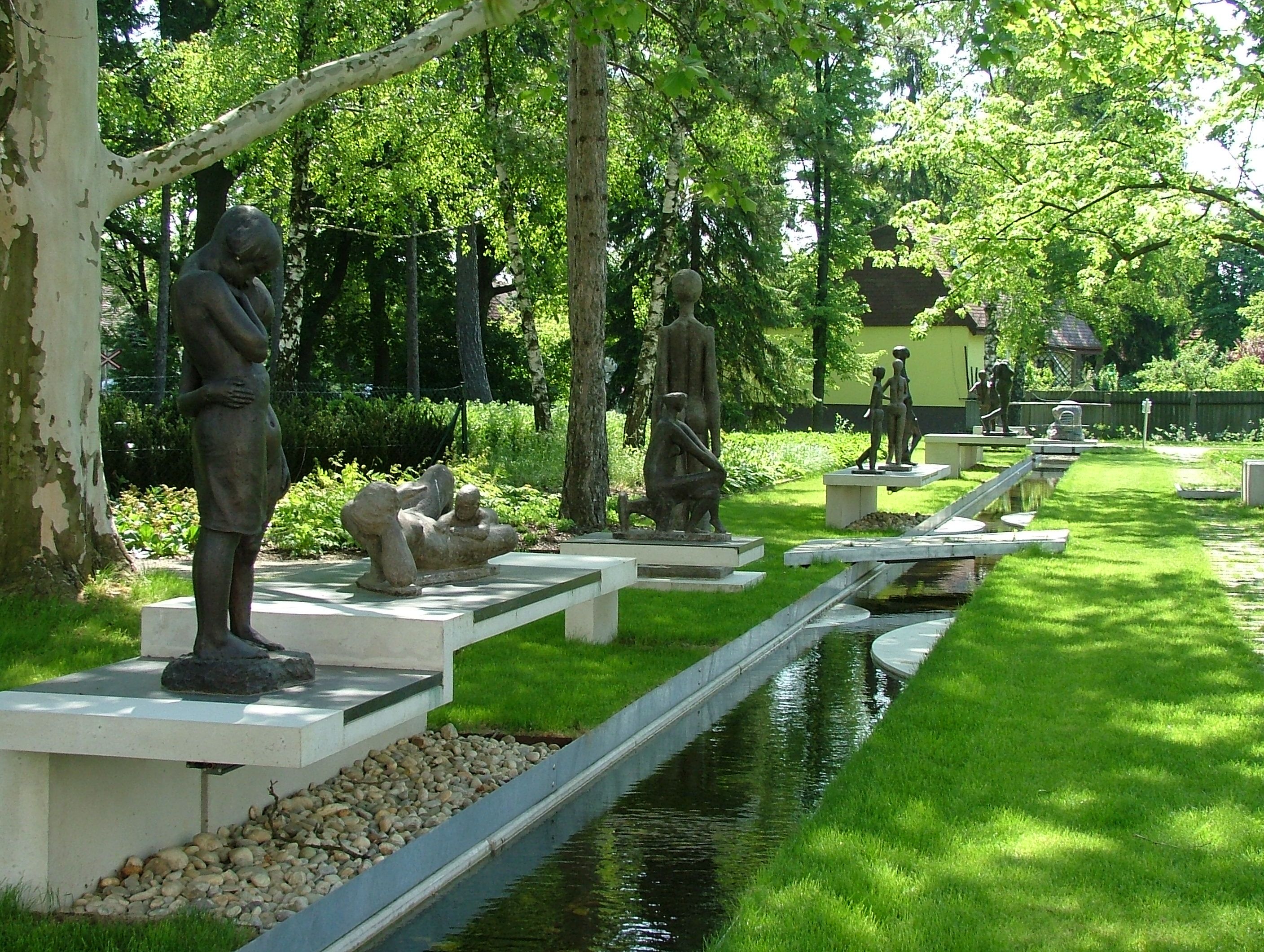 Sculptures in the park of Bad Pirawarth, surrounded by trees and a small stream.