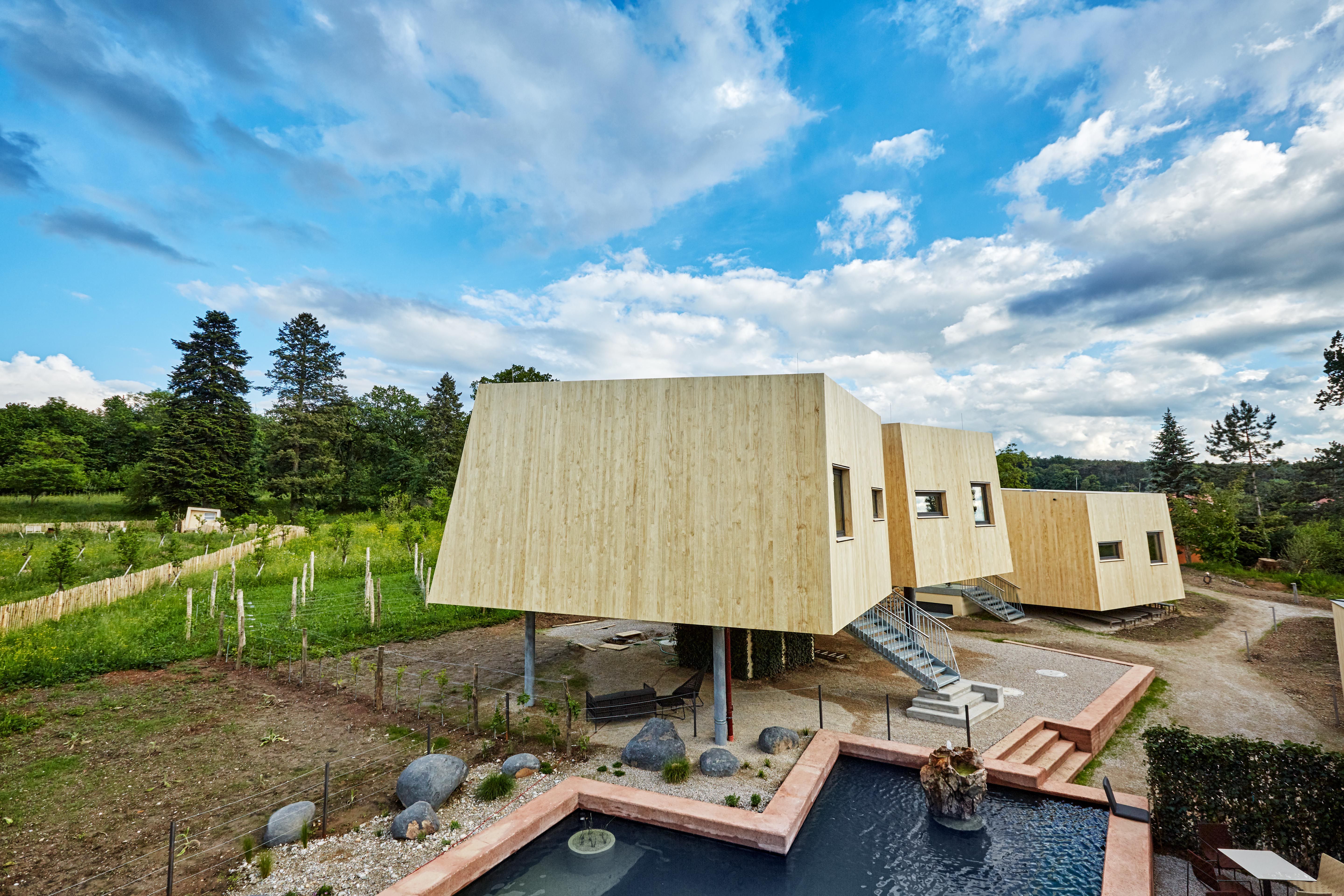 Modern wooden garden lofts with steps, surrounded by nature and a pond in the foreground.